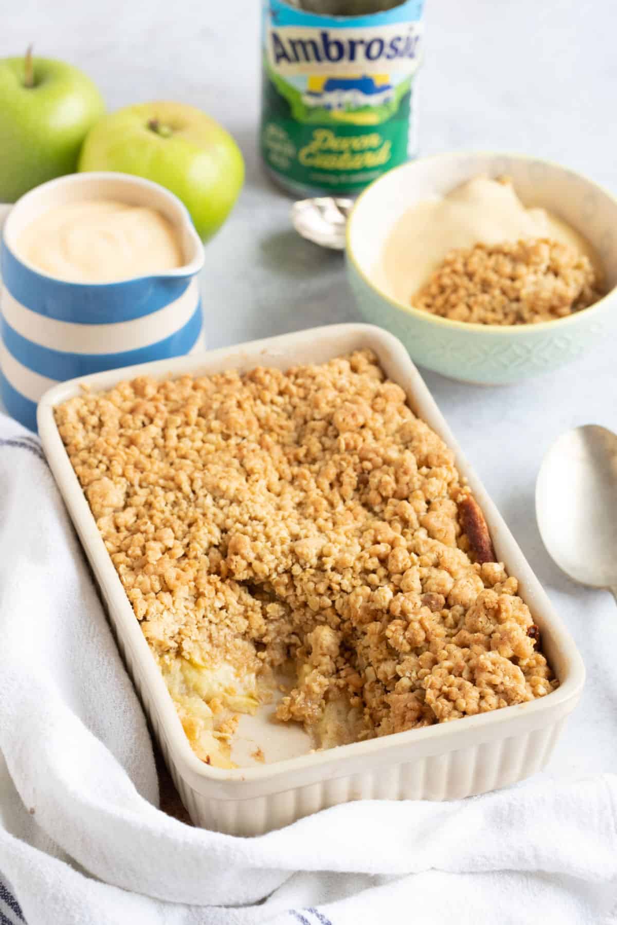 Air fryer apple crumble in a baking dish with a jug of custard.