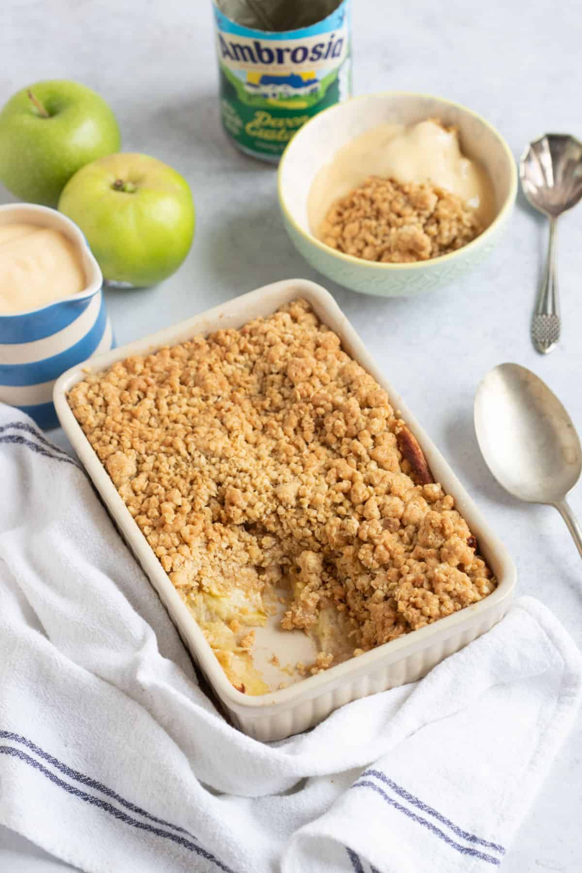 Apple crumble in a baking dish with a jug of custard.