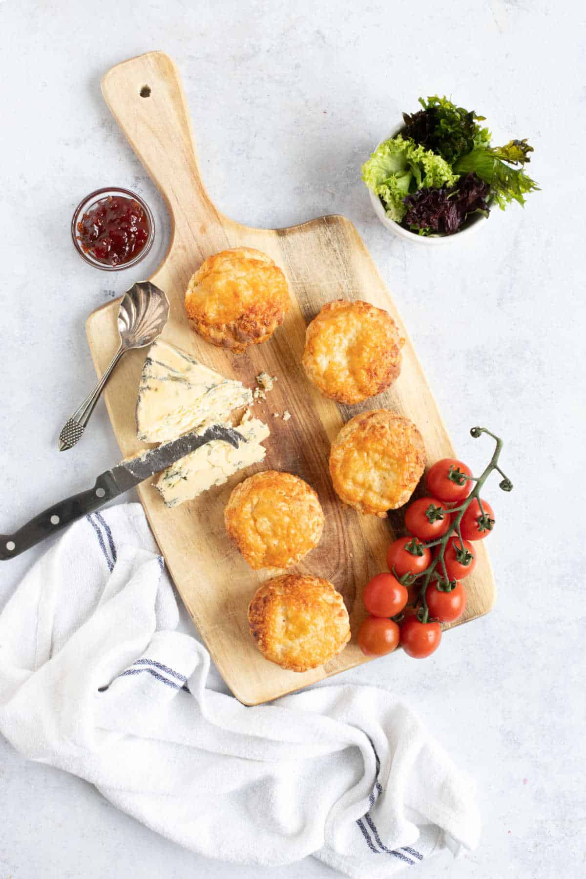 Cheese scones on a wooden board with cherry tomatoes and chutney.