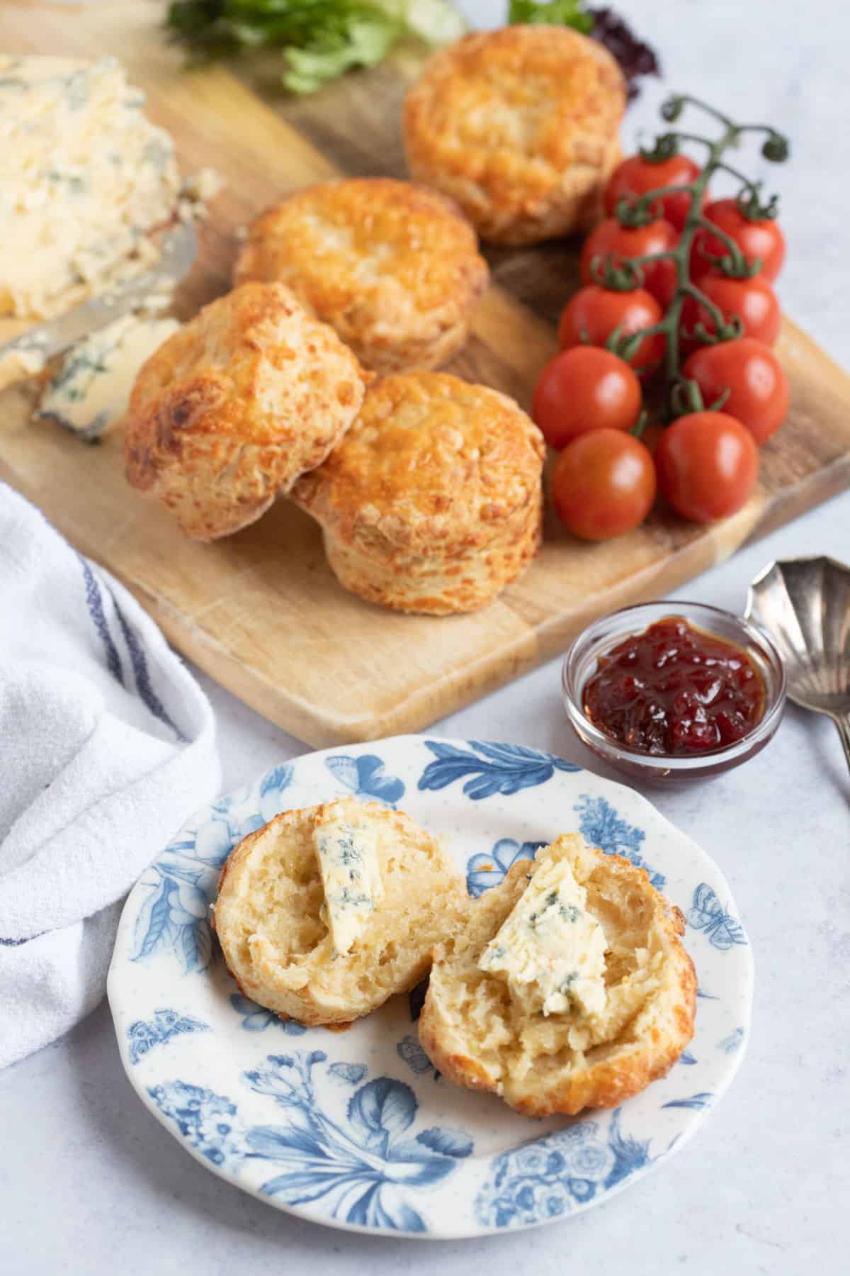 A cheddar cheese scone split in half on a blue and white plate and topped with cheese slices.