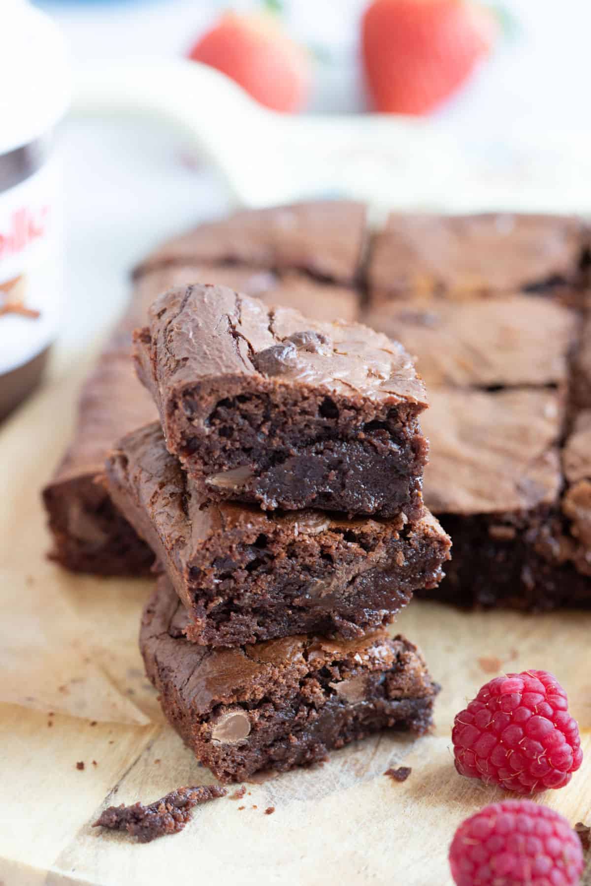 A stack of air fryer brownies on a wooden board with fresh raspberries.