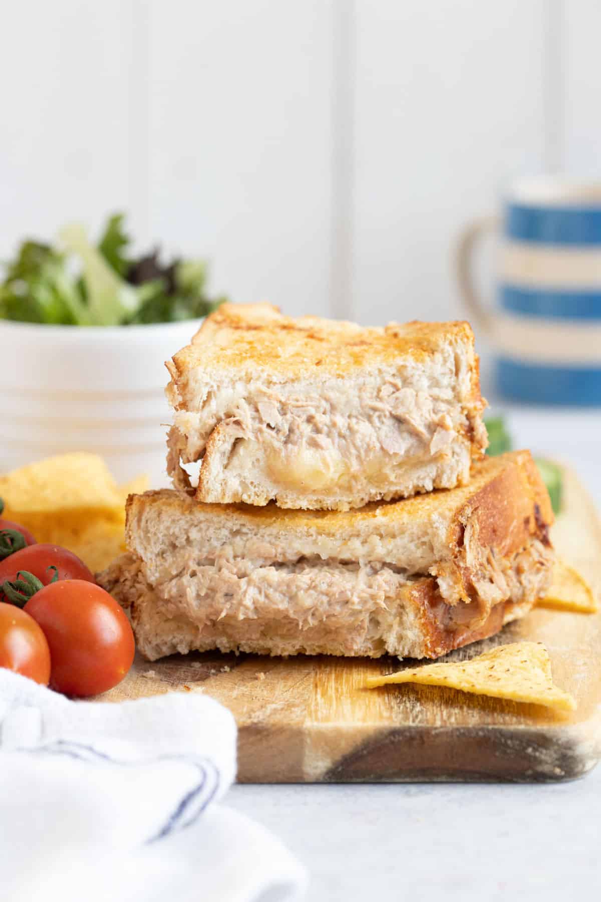 Air fryer tuna melt sandwich on a wooden board with cherry tomatoes, cucumber and salad.