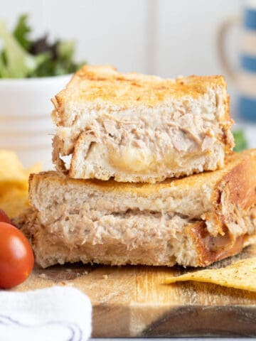 Air fryer tuna mwlt sandwich on a wooden board with salad and crisps.