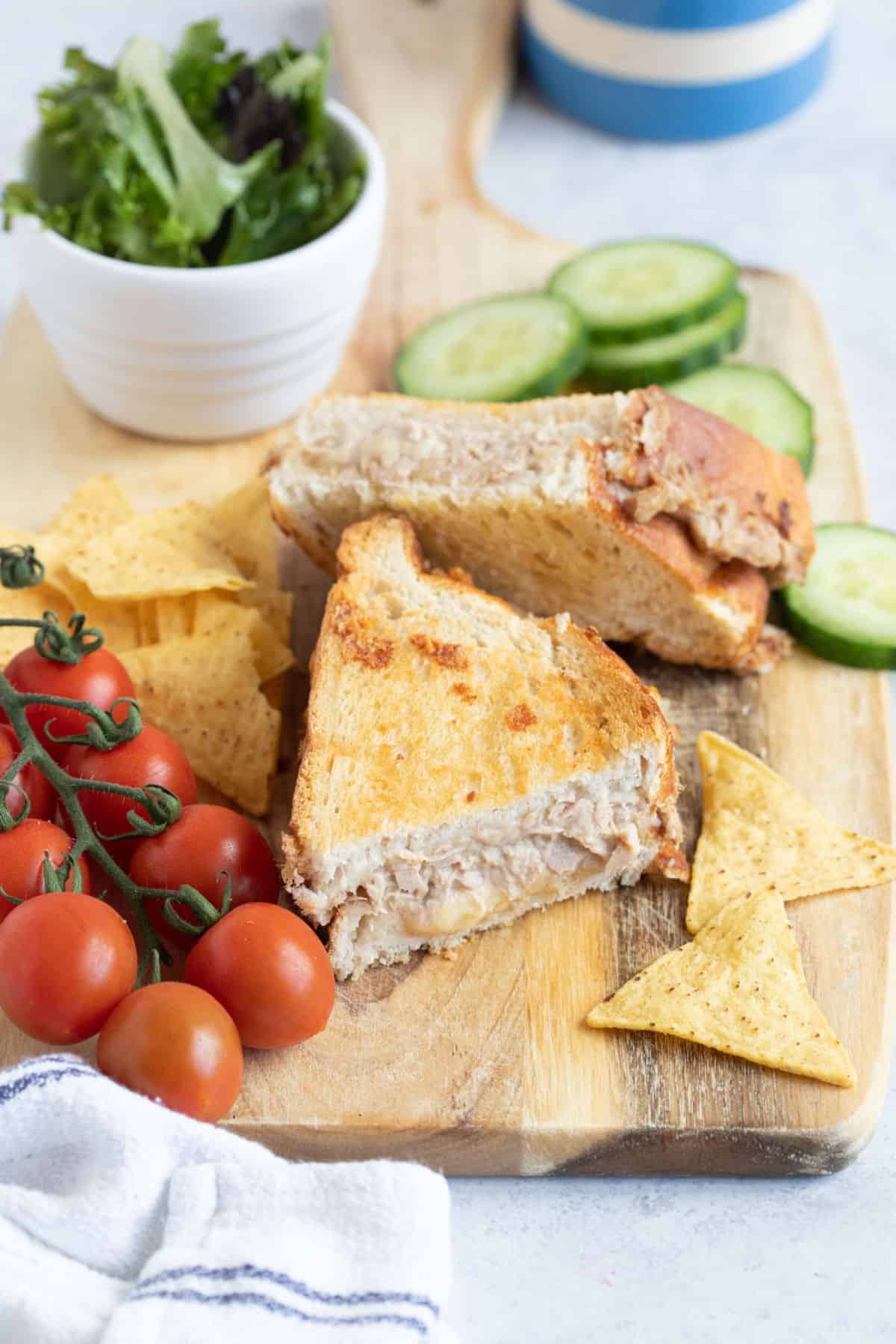 An air fryer tuna melt on a wooden board with salad vegetables.