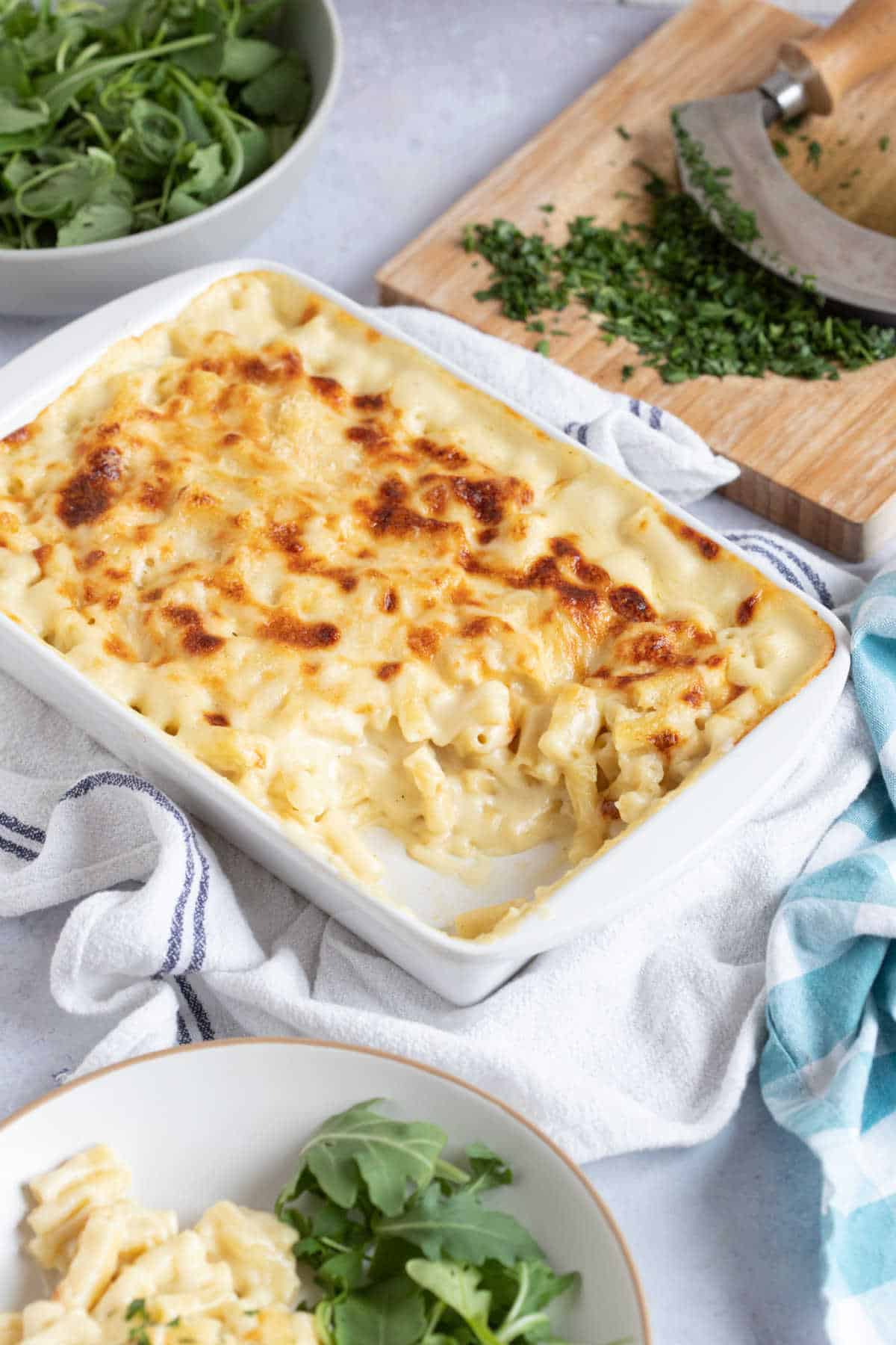 Macaroni cheese in a rectangular baking dish with a green salad behind it.