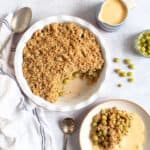 Gooseberry crumble in a round pie dish with a jug of custard.