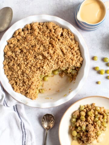 Gooseberry crumble in a round pie dish with a jug of custard.