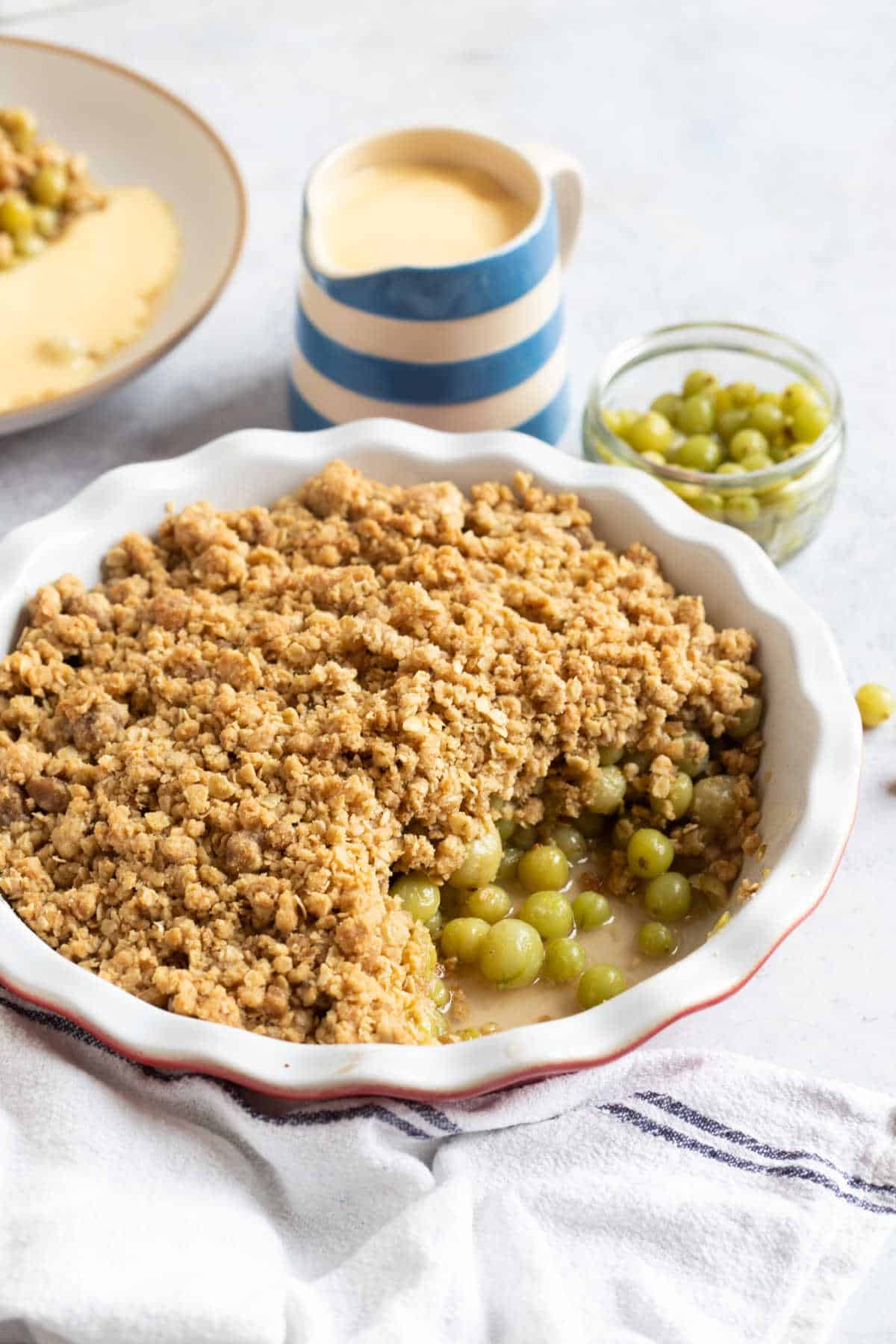 Gooseberry crumble in a red and white pie dish with a jug of custard.