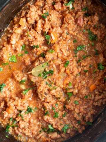 Slow cooker pork ragu in a black crock pot.