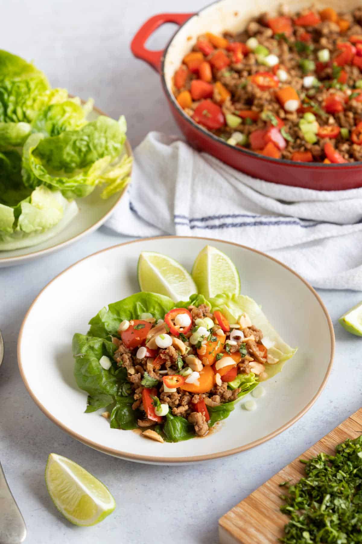 Chinese lettuce wraps on a white plate with lime wedges and chilli.