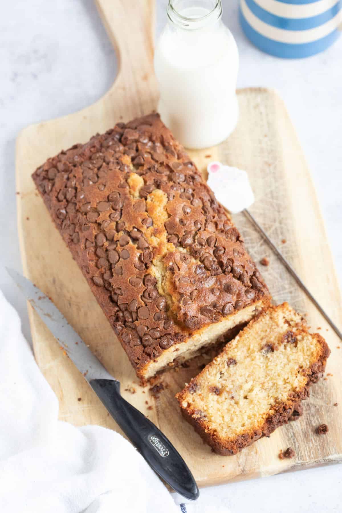 Chocolate chip banana bread on a wooden board with a glass of milk in the background.