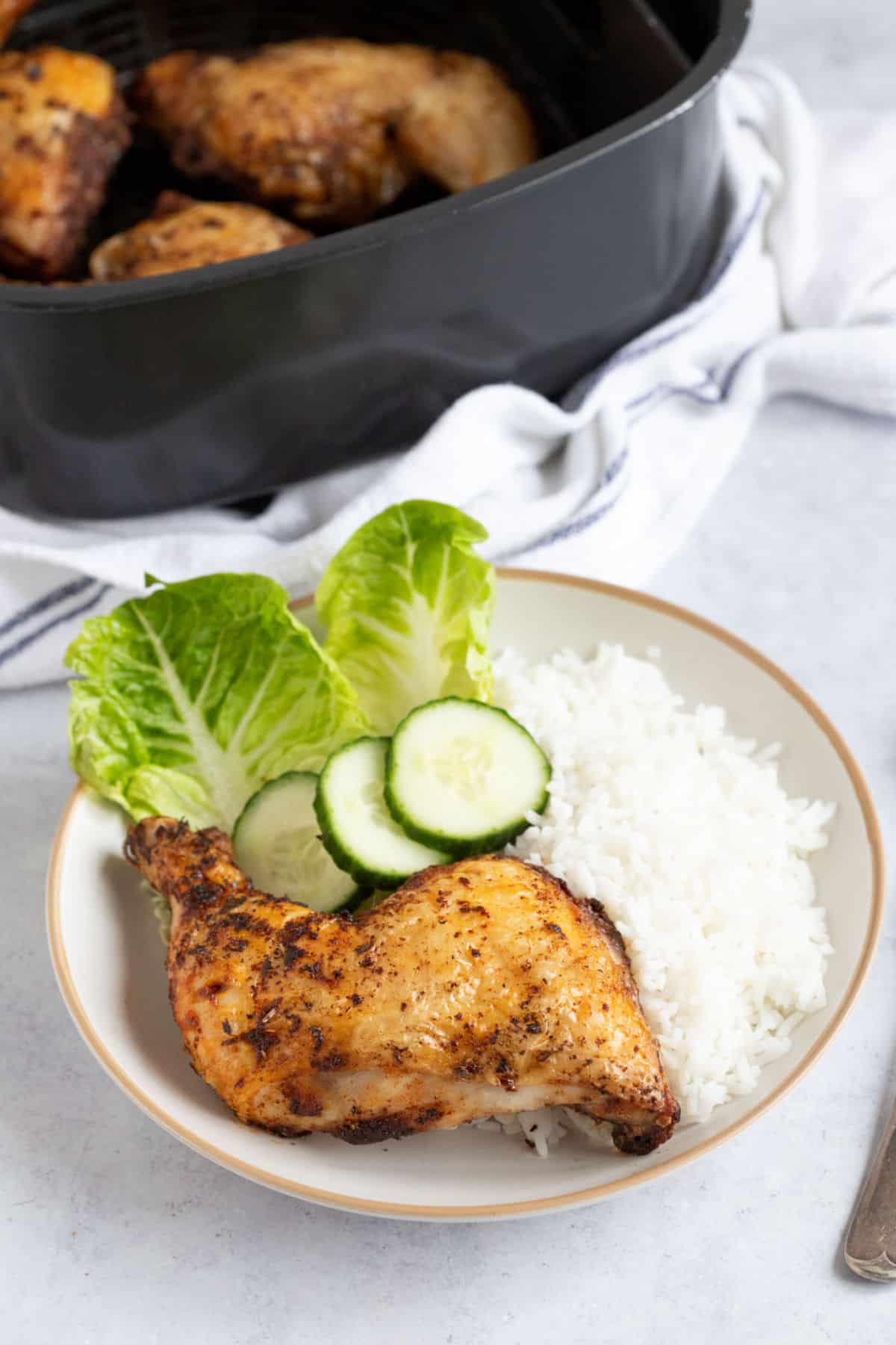 A crispy air fryer chicken leg on a plate with rice and salad.