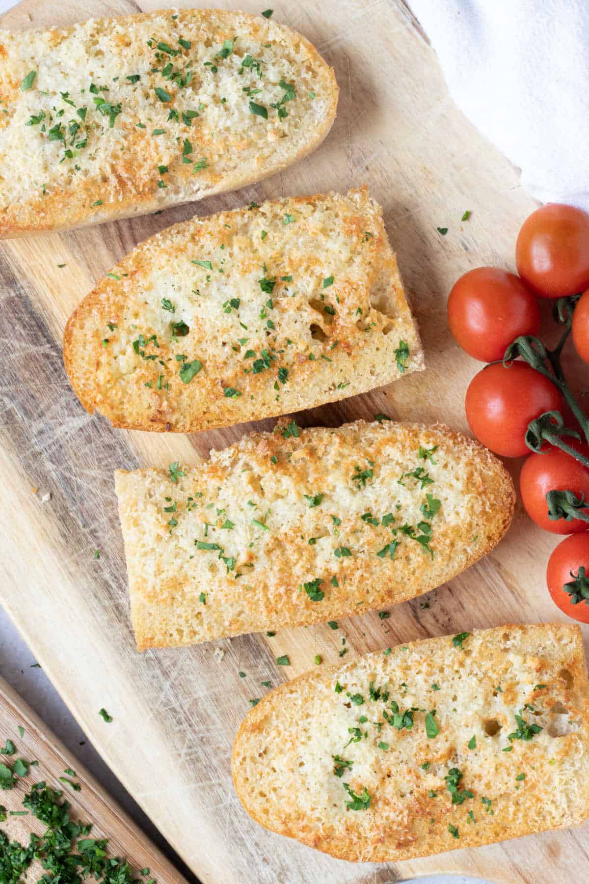 Air fryer garlic bread on a wooden board with cherry tomatoes.