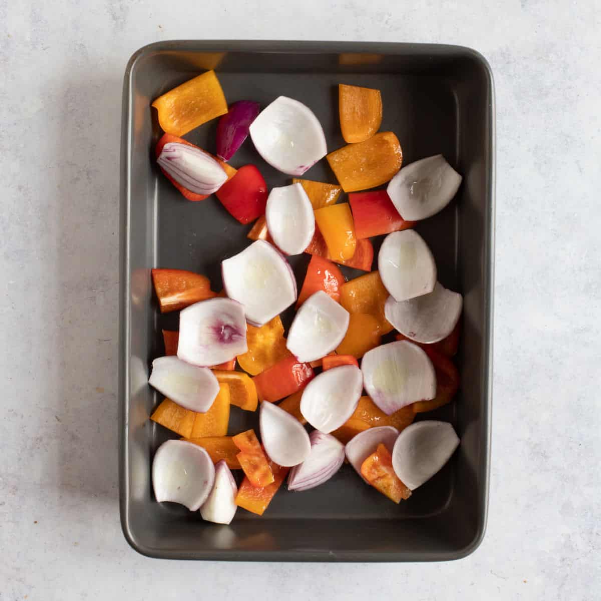 Chopped peppers and onions in the bottom of a roasting tin.