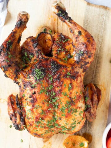 Harissa roast chicken on a wooden carving board.