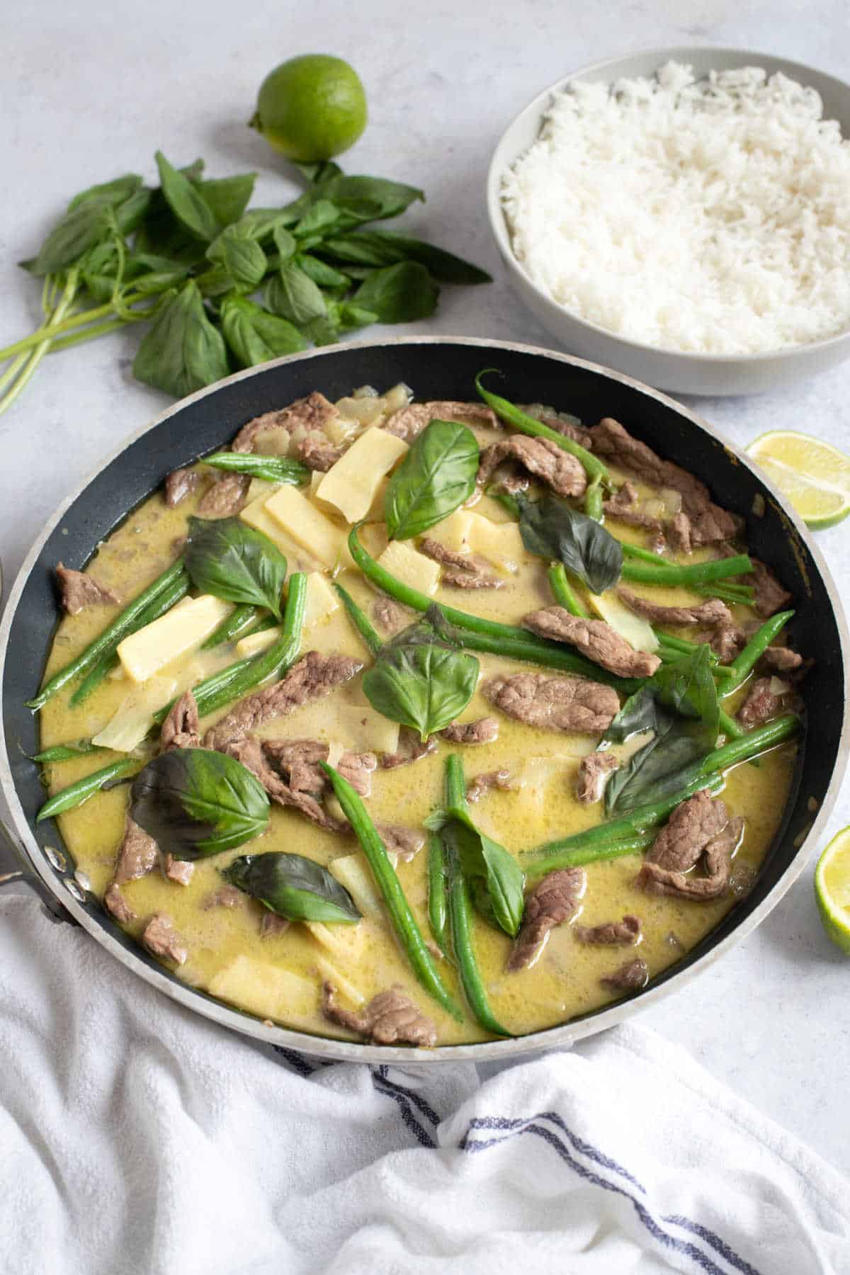 Thai green beef curry in a pan with a side of rice and lime wedges.