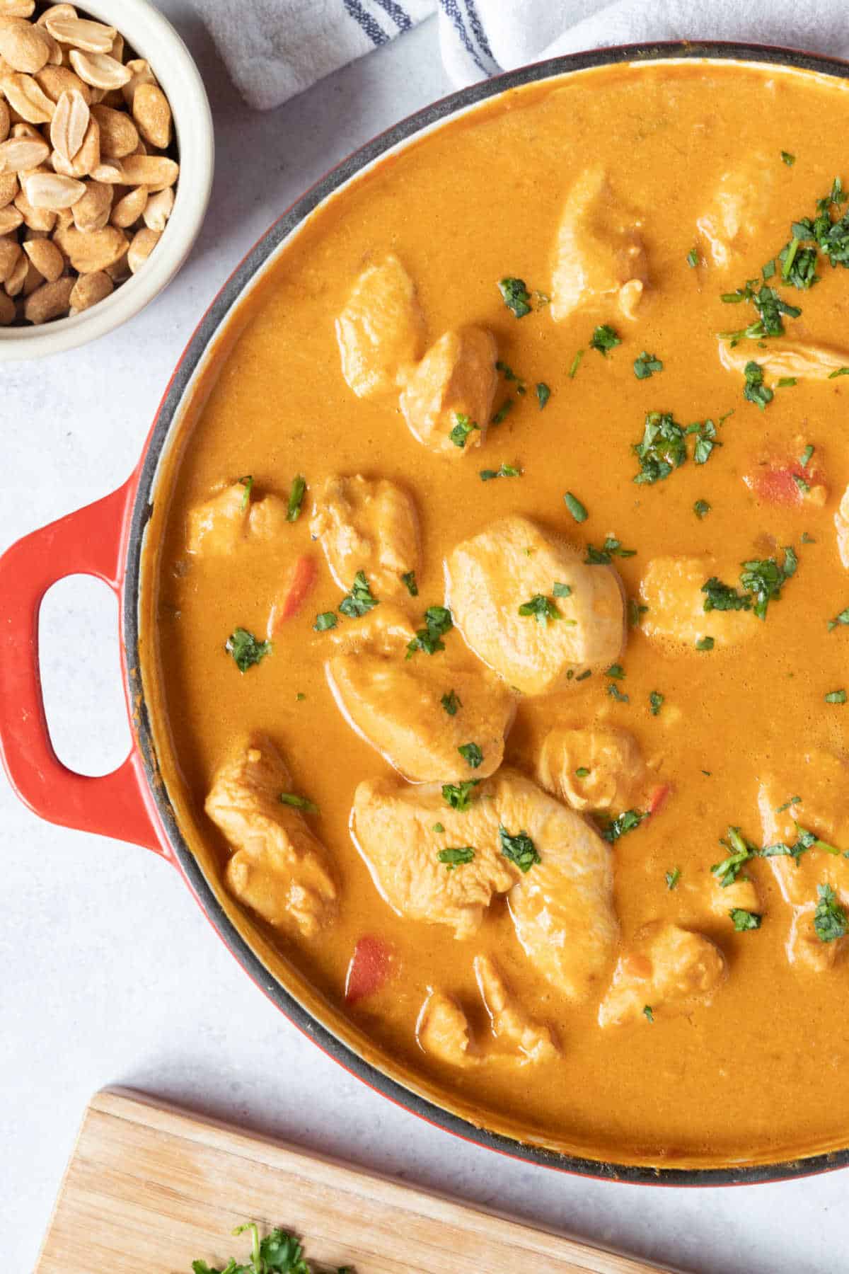 A pan or peanut butter chicken curry with a small bowl of salted peanuts on the side.