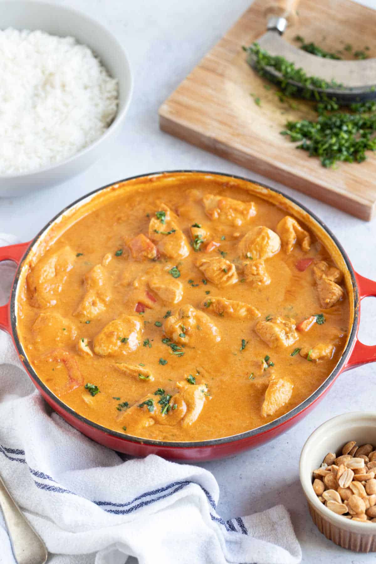 Peanut butter curry in a red pan with a bowl of rice and chopped coriander.