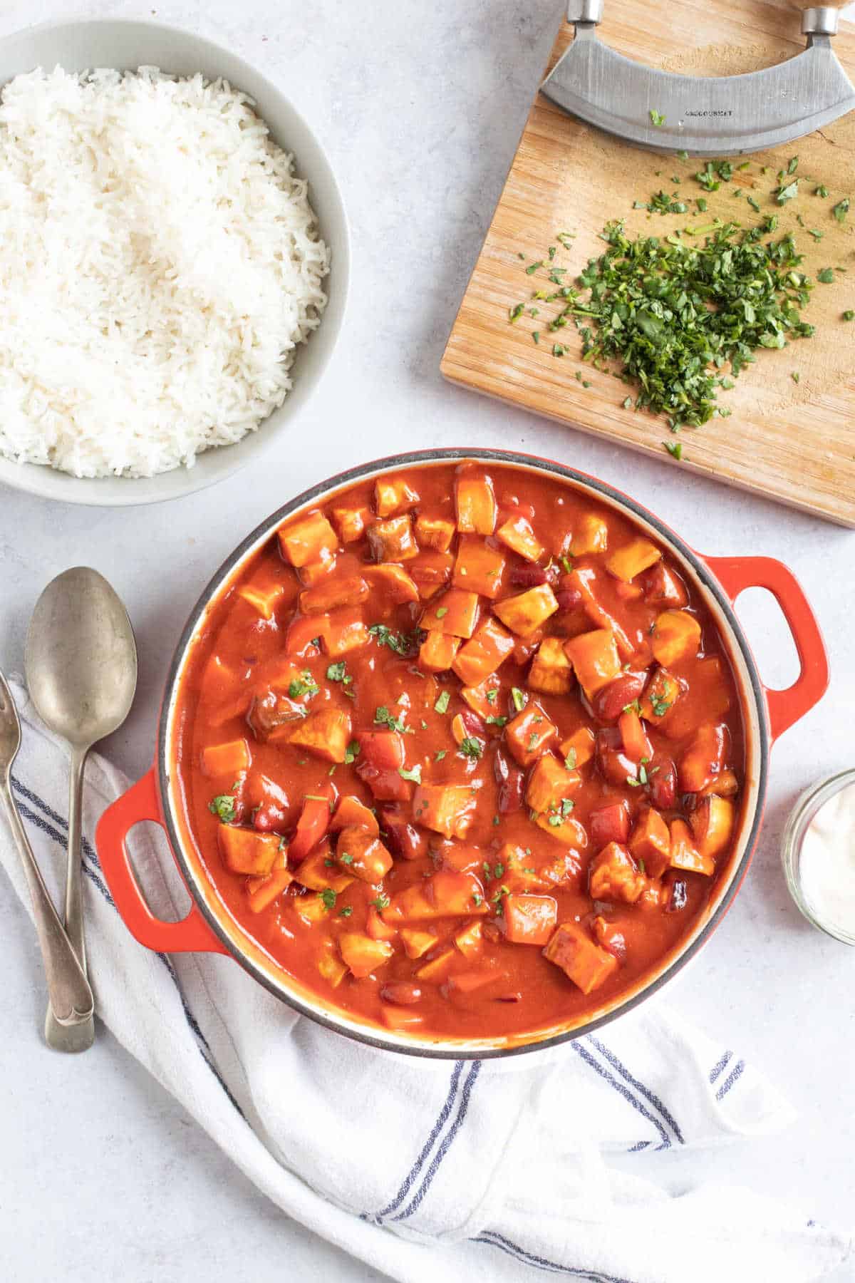 A pan of kidney bean and sweet potato chilli with a bowl of rice and chopped coriander on the side.