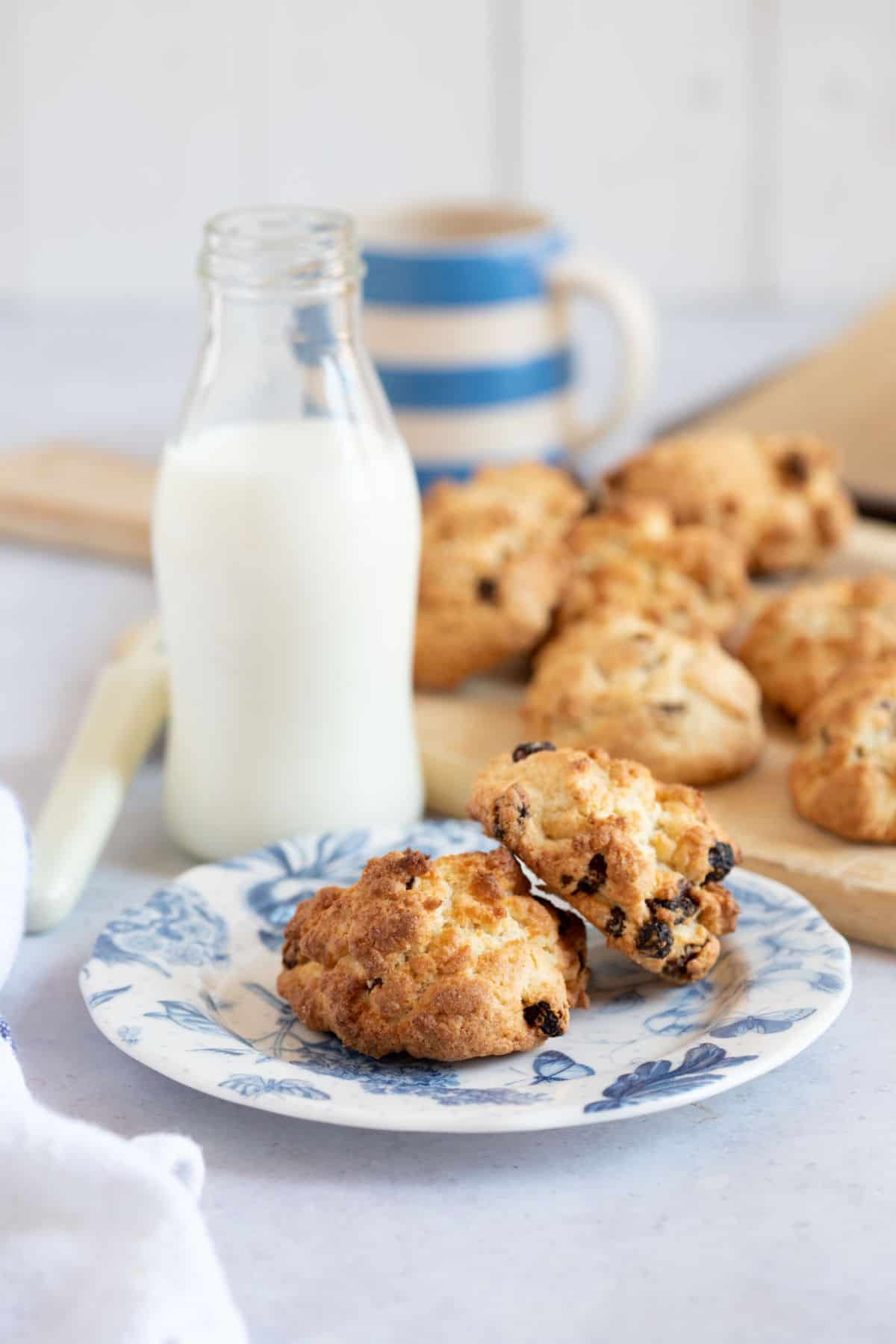 Two rock cakes on a blue and white plate with a glass of milk behind.