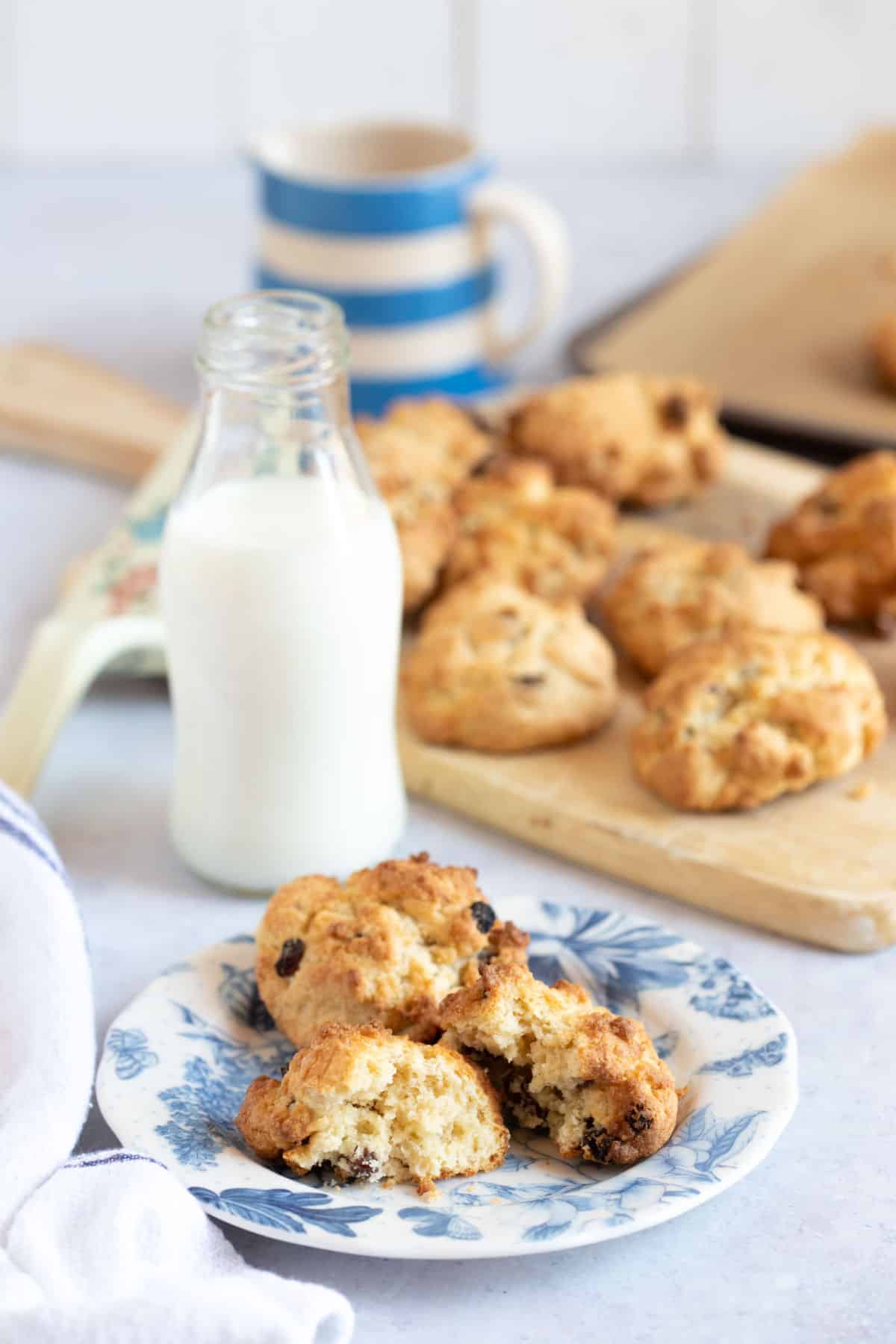 Rock buns on a plate with a glass of milk behind.