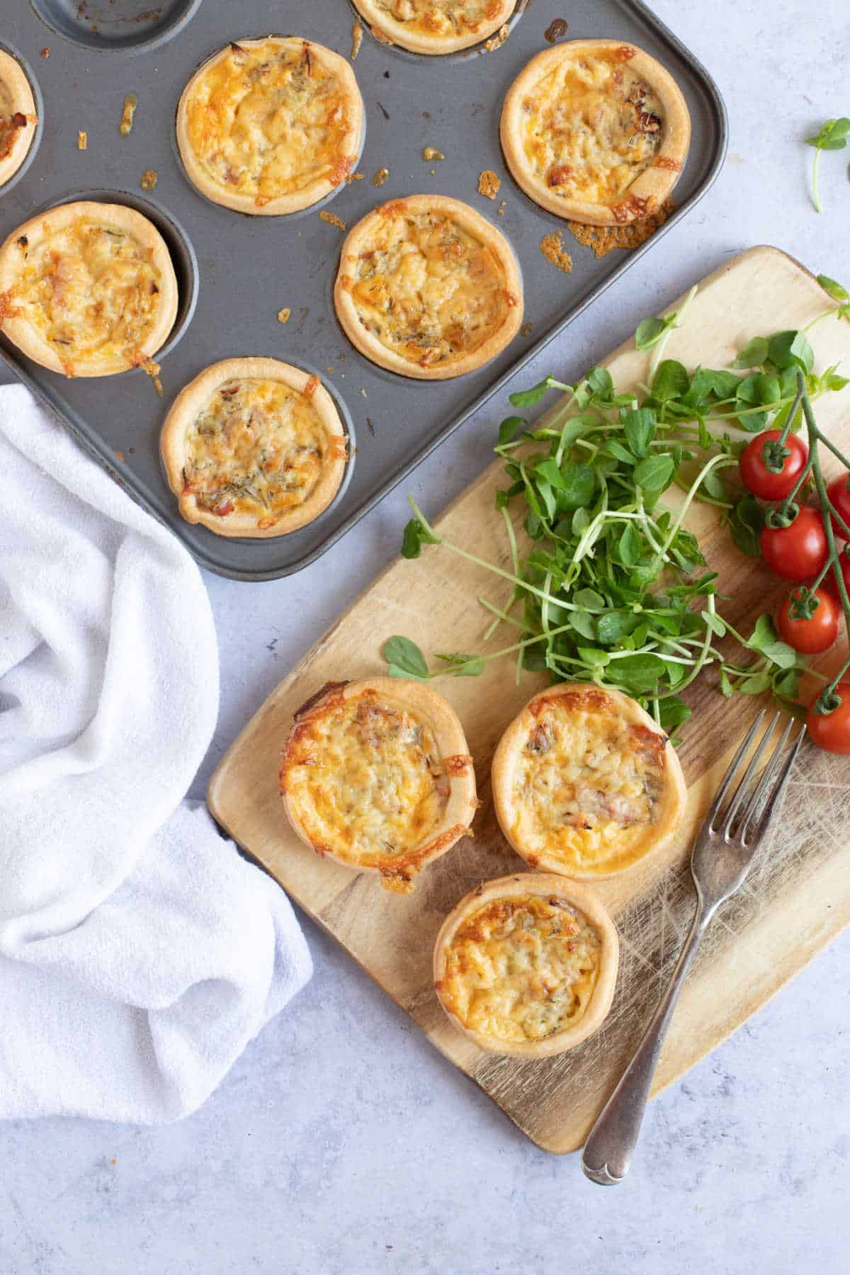 Three mini quiches on a wooden board with cherry tomatoes and watercress.