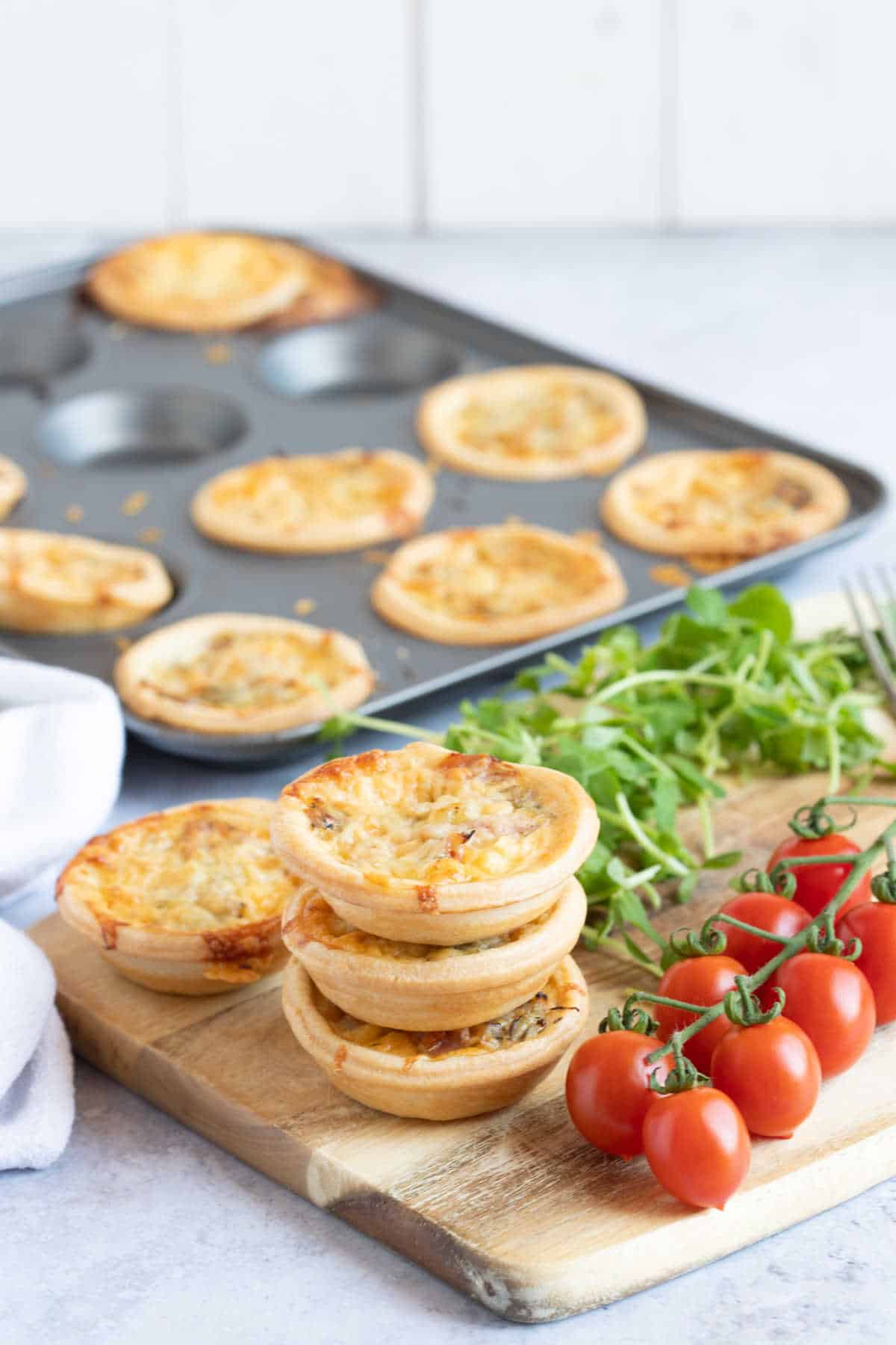 A stack of mini ham and cheese quiches on a wooden board.