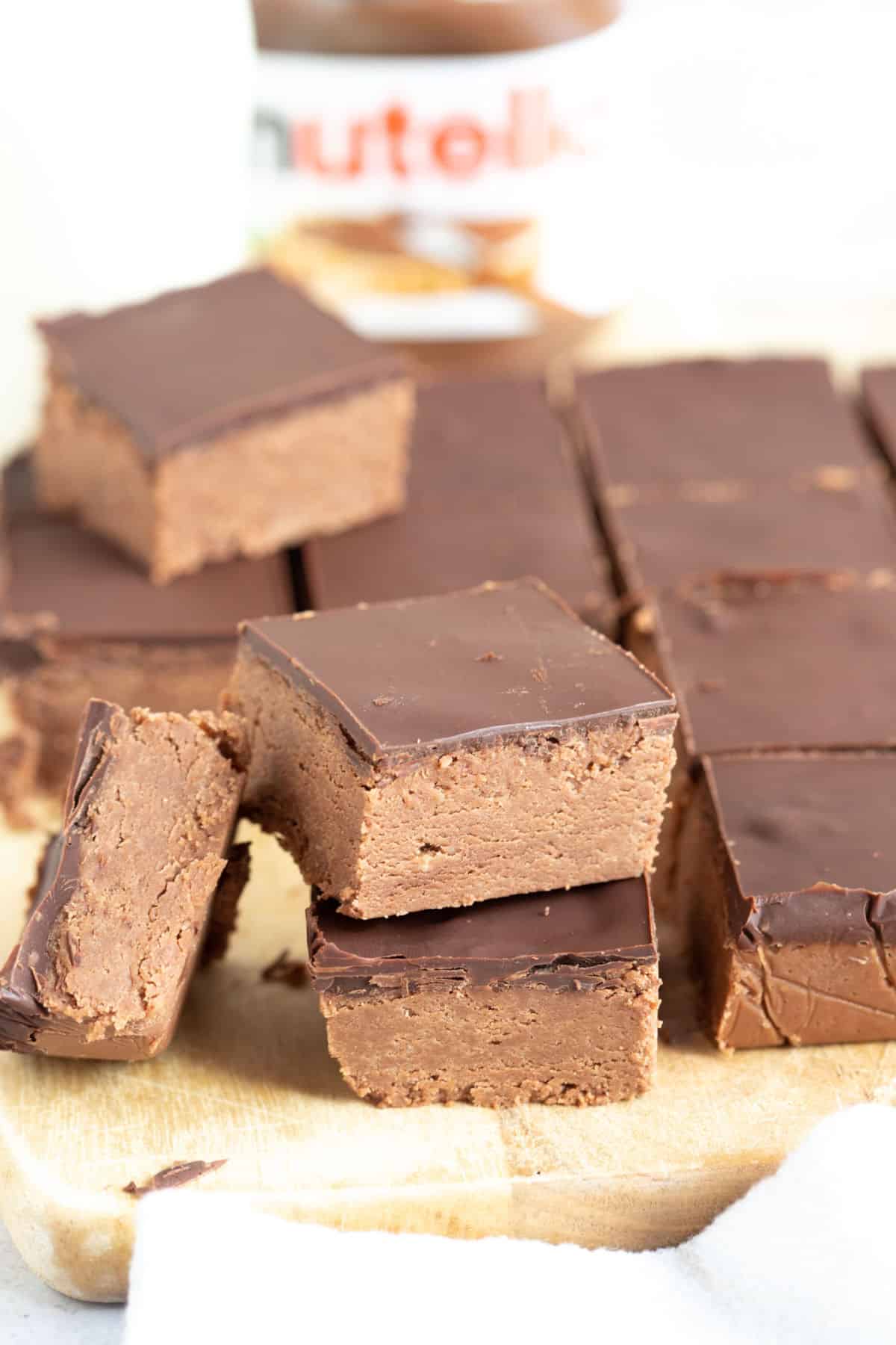 A stack of no bake chocolate Nutella biscuit squares with a jar of Nutella behind.