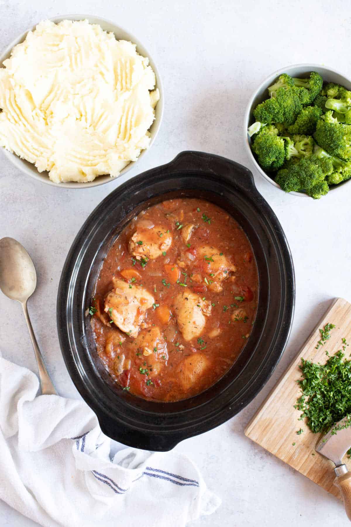 Chicken chasseur in a slow cooker with a side of mashed potatoes and broccoli.