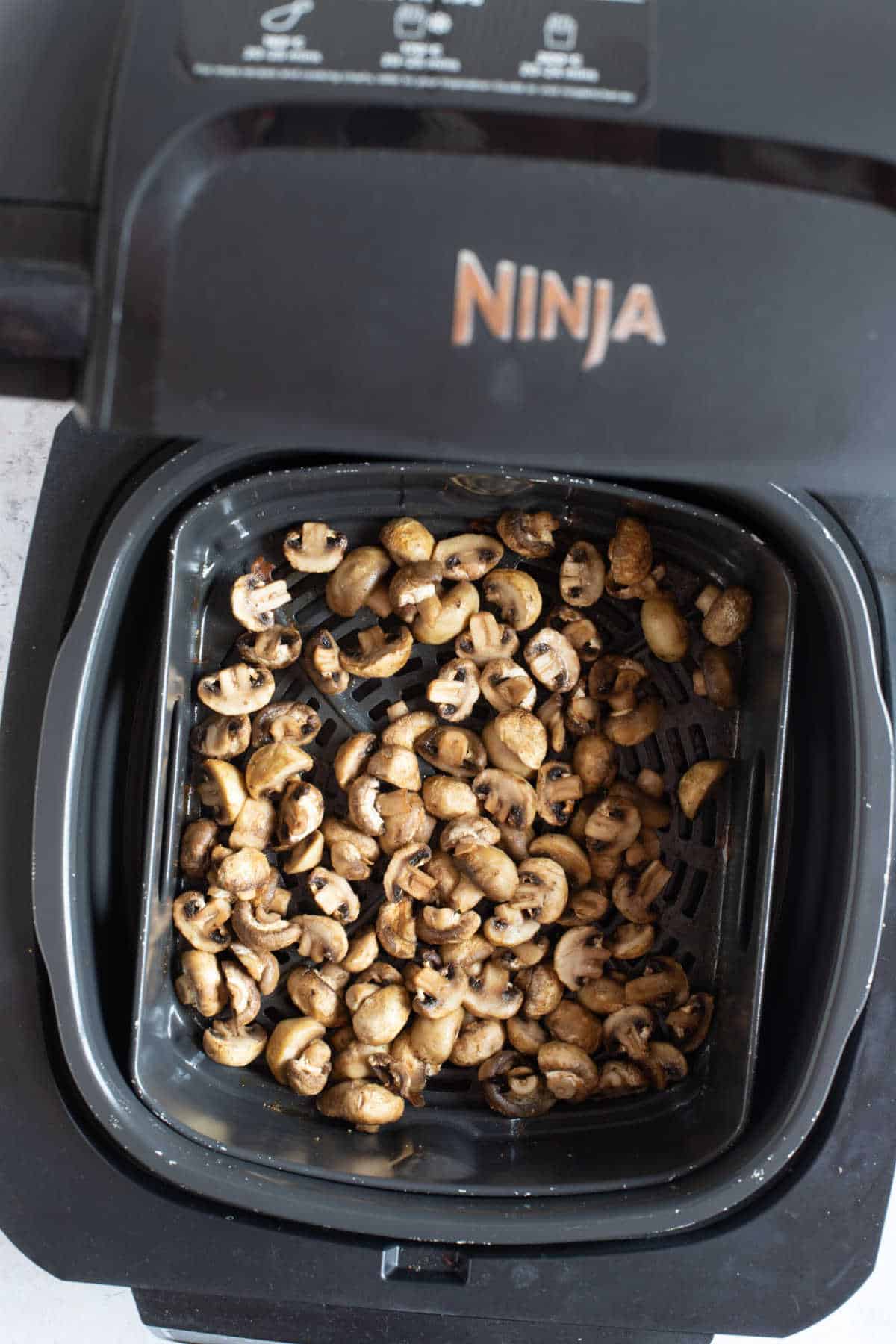 Halved button mushrooms in an air fryer.