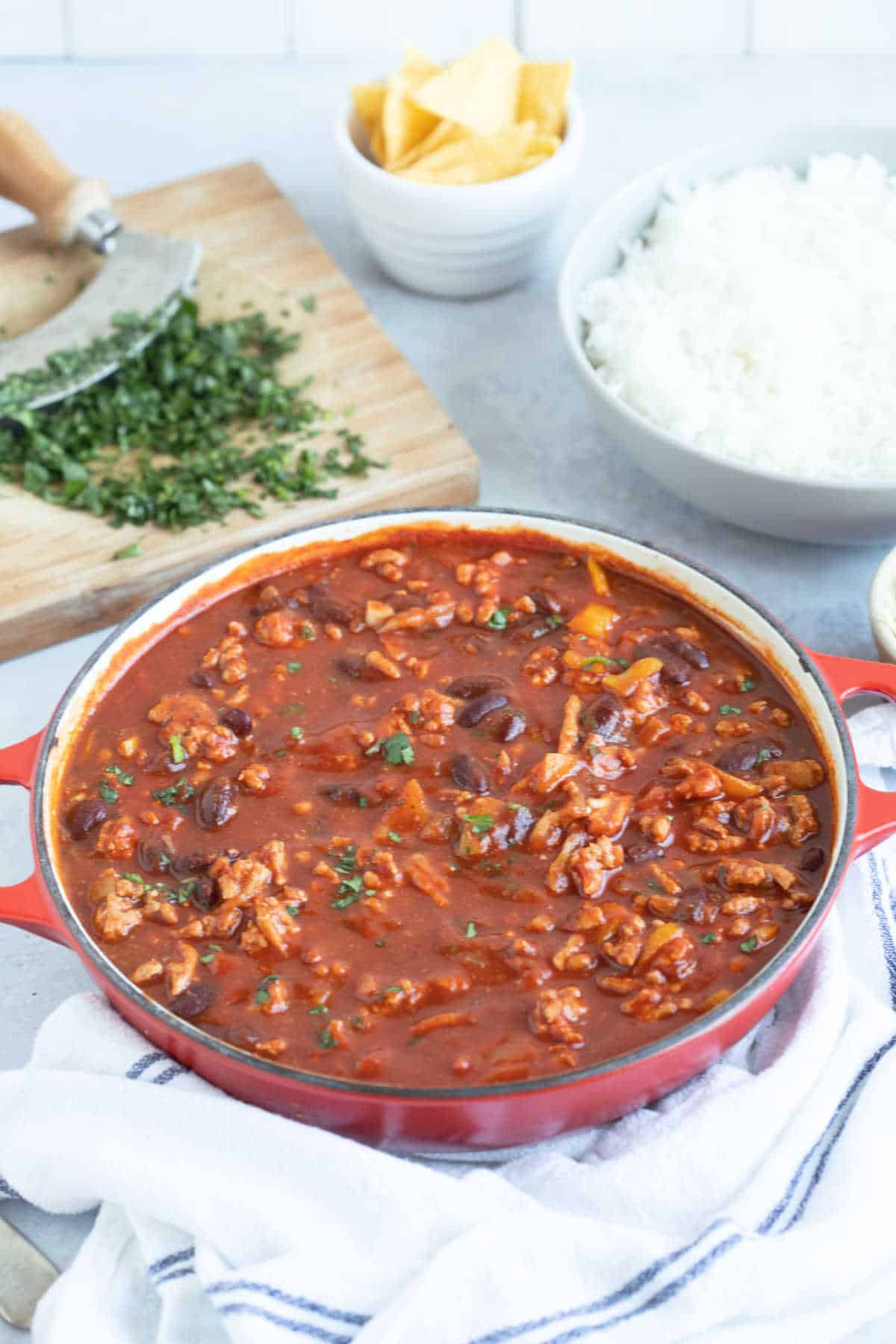 A bowl of turkey mince chilli with coriander, rice and tortilla chips on the side.