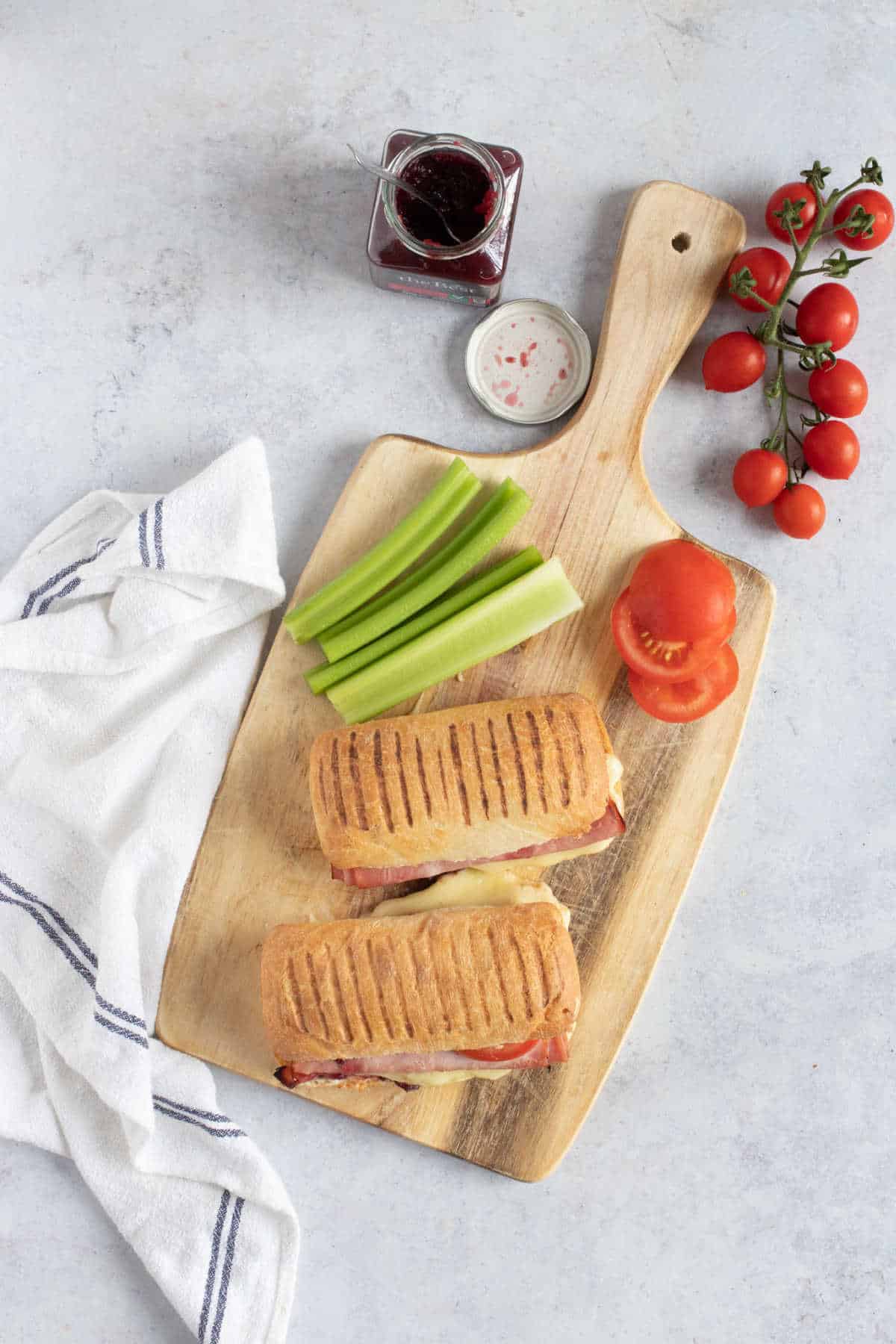 Two panini rolls on a wooden board with celery sticks.