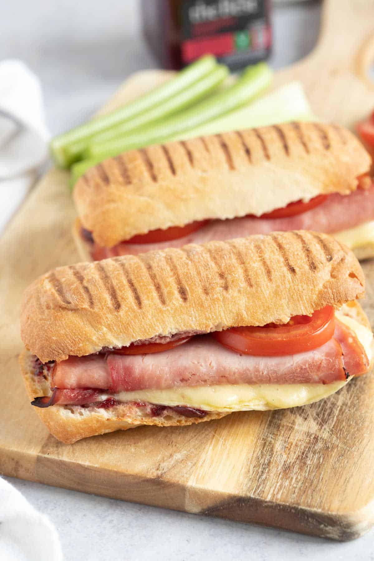 Two ham and cheese paninis on a wooden board.