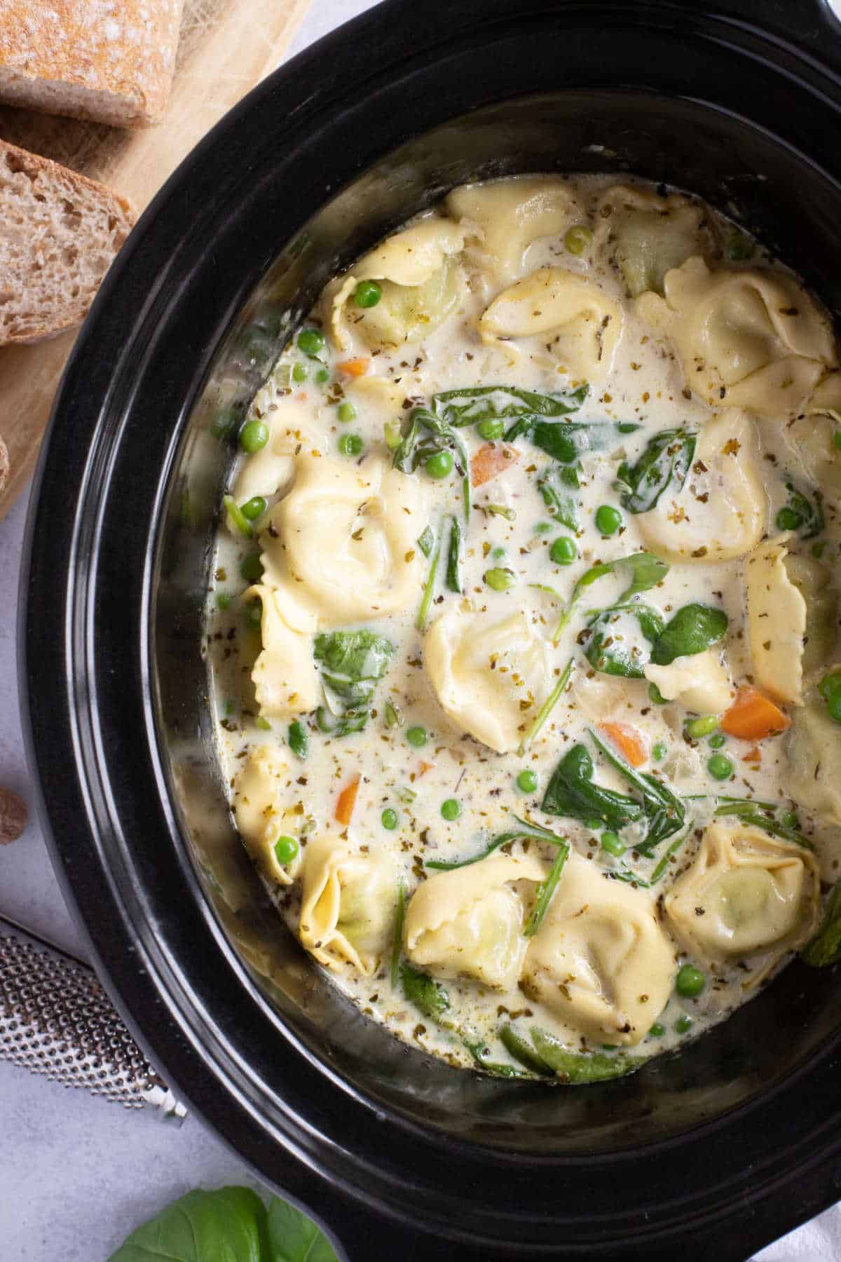 Slow cooker tortellini soup in black crockpot.