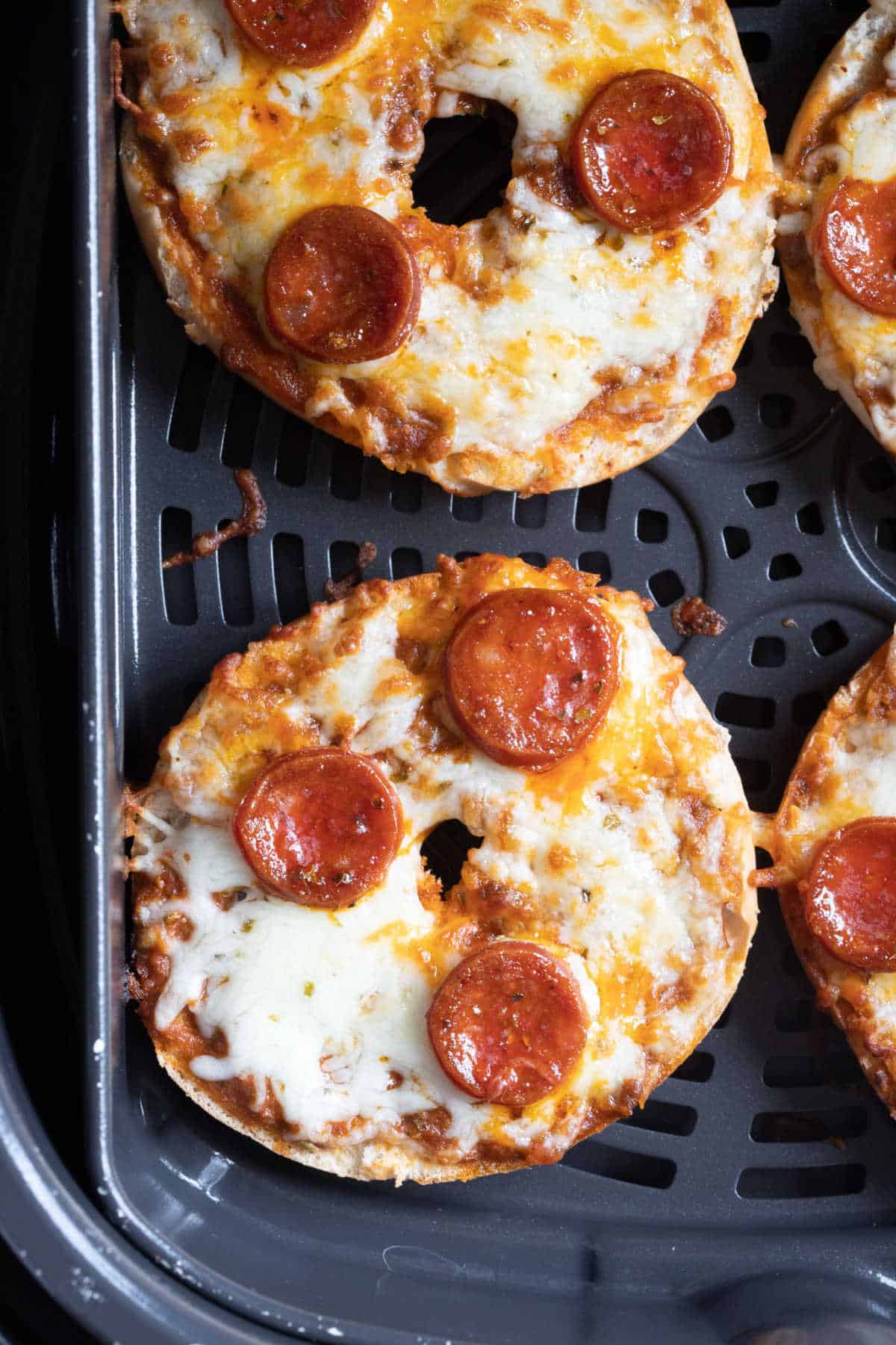 Pizza bagels in an air fryer basket.