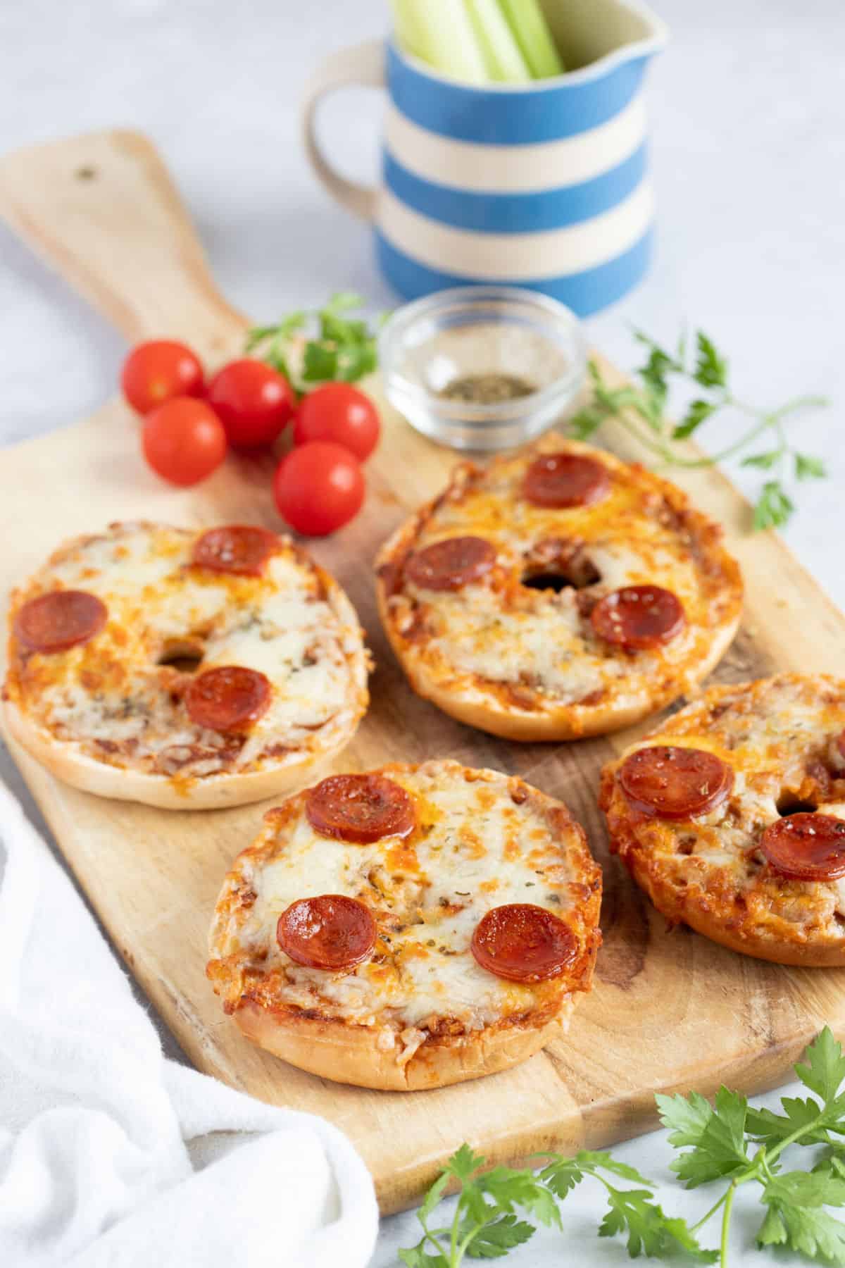 Air fried bagel pizzas on a wooden serving board with cherry tomatoes.