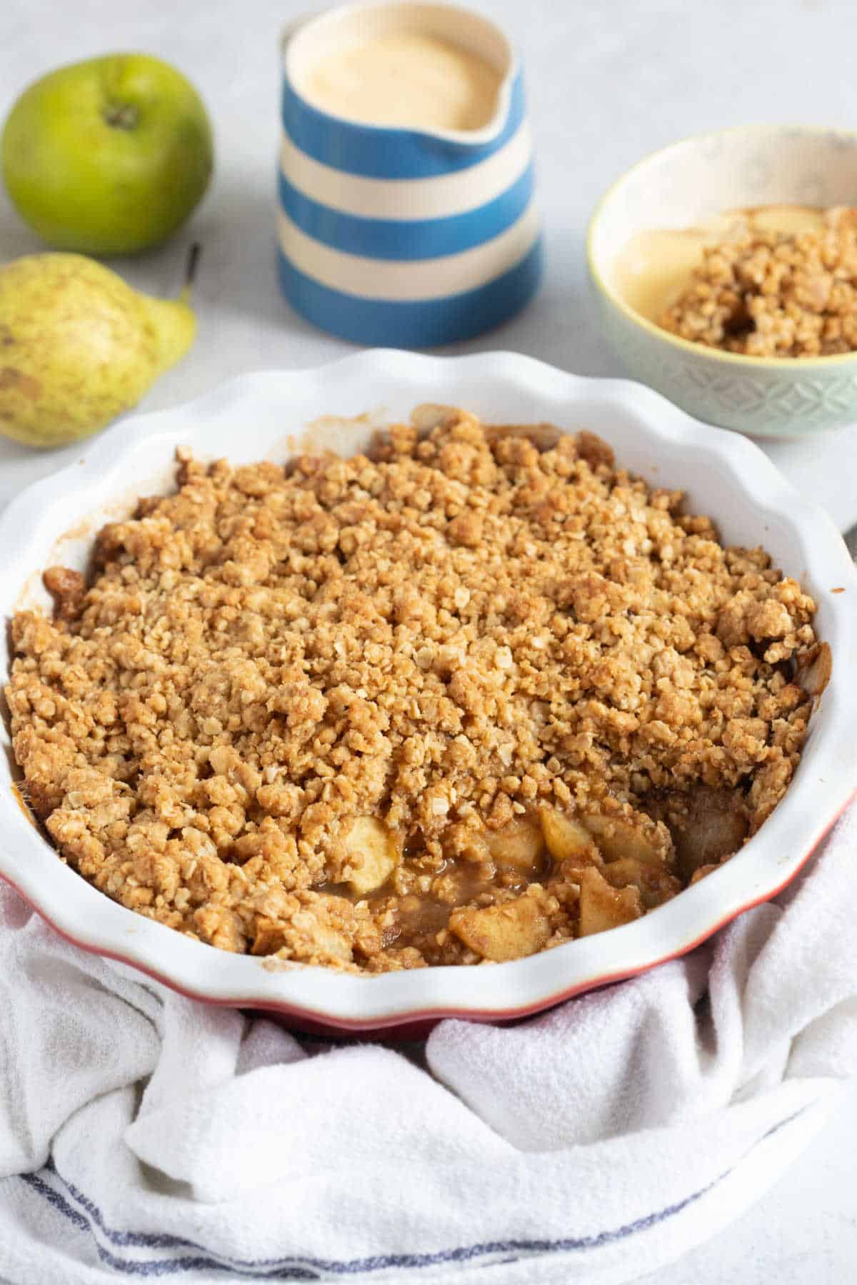 Apple and pear crumble in a red pie dish with a crispy oat topping.