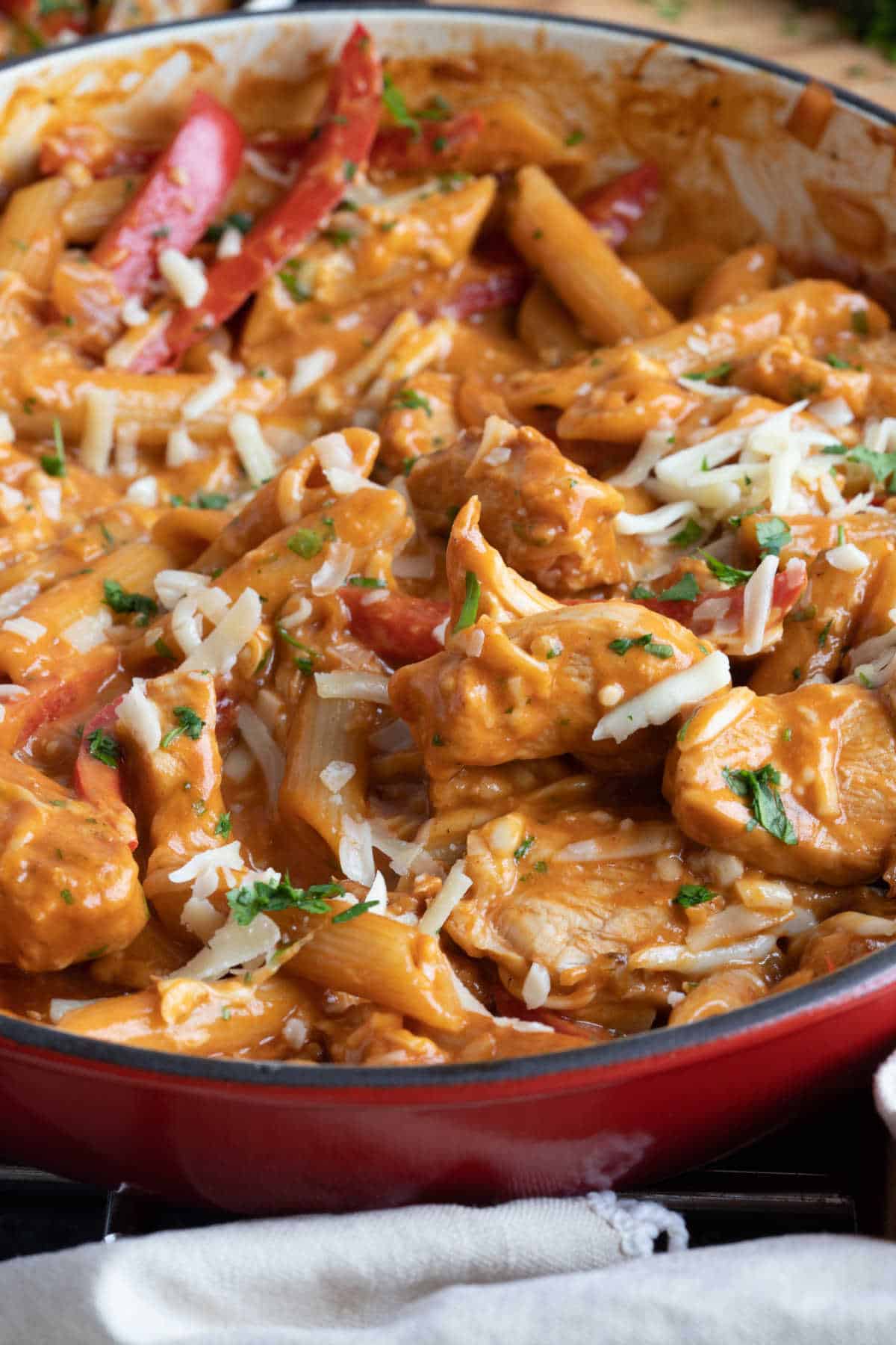 Barbecue chicken pasta in a red pan with grated cheese on top.