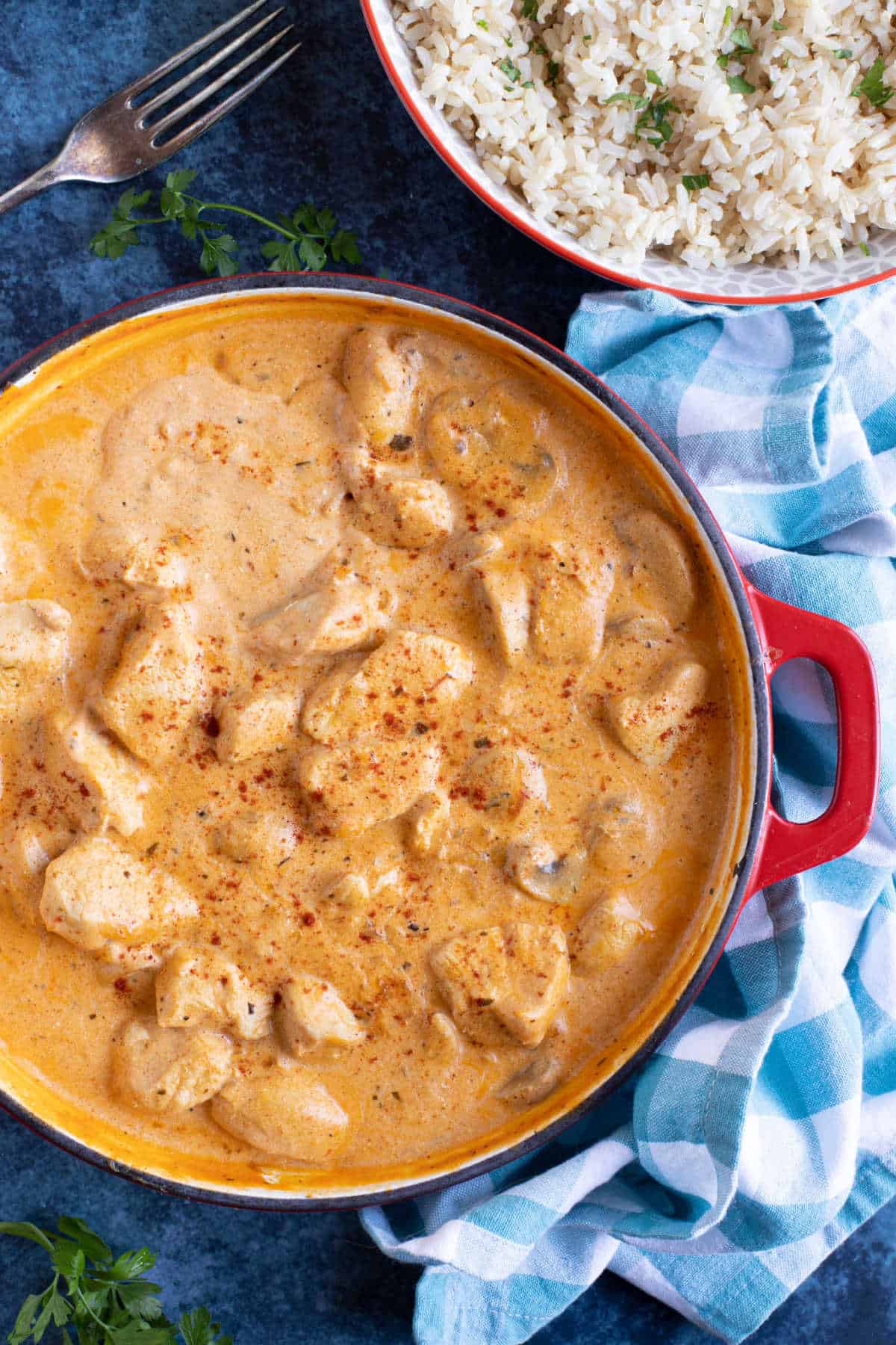 Chicken and mushroom stroganoff in a red pan with a bowl of rice on the side.