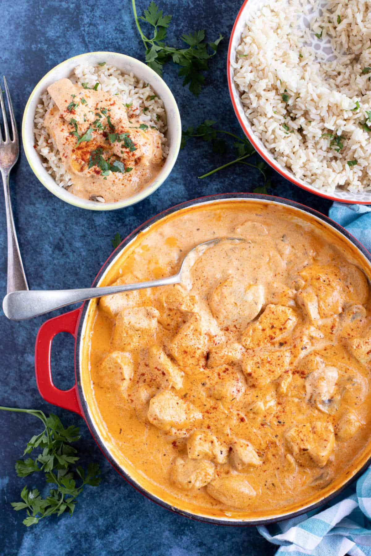 Chicken and mushroom stroganoff in a pan with a bowl of stroganoff and rice on the side.