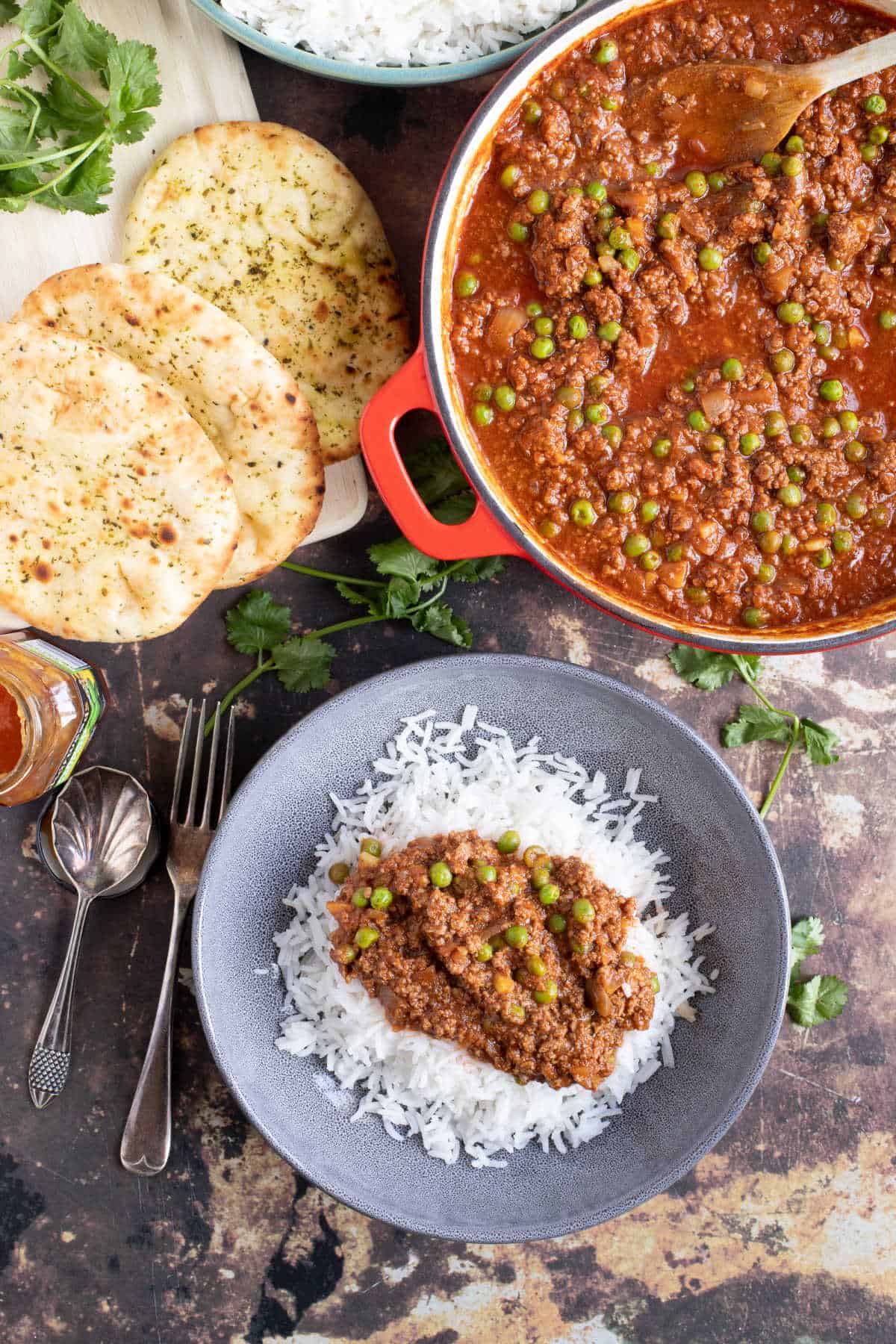 A bowl of minced beef keema curry with basmati rice with a pan of keema curry and naan breads.