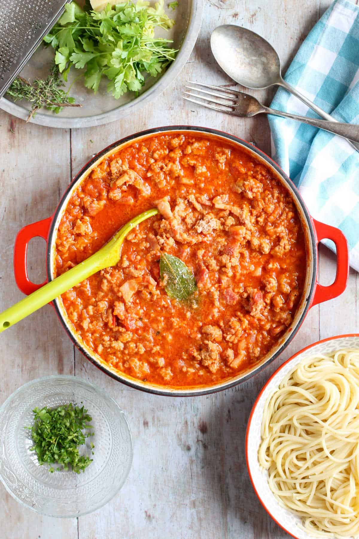 A pan of pork mince bolognese with a bowl of spaghetti on the side.
