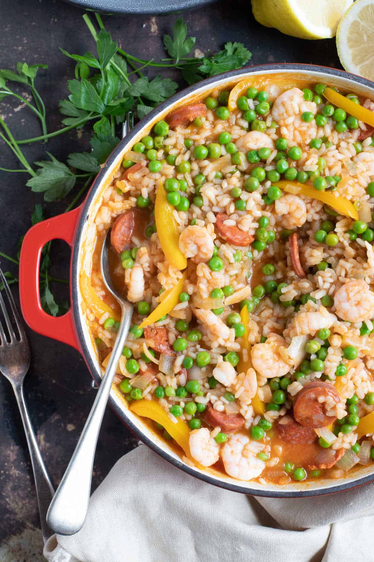 Prawn paella with peas and chorizo in a red pan.