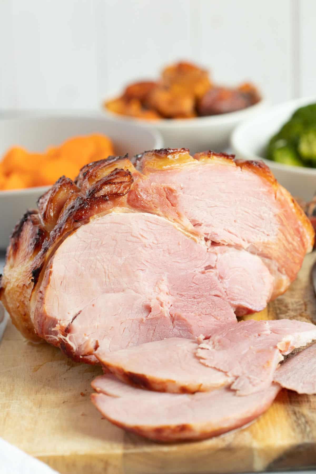 Slow cooker gammon joint on a wooden carving board with some thick slices cut.