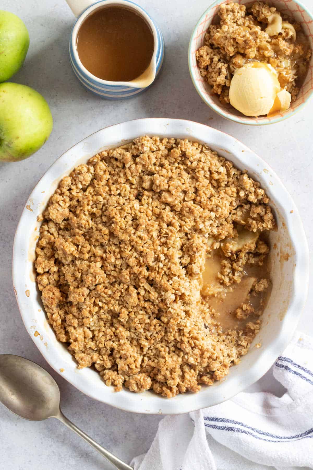 Warm toffee apple crumble served with vanilla ice-cream and extra toffee sauce in an autumn setting.