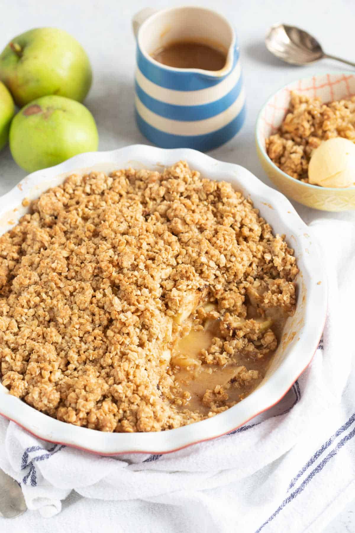 Toffee apple crumble in a red pie dish with a jug of toffee sauce on the side.