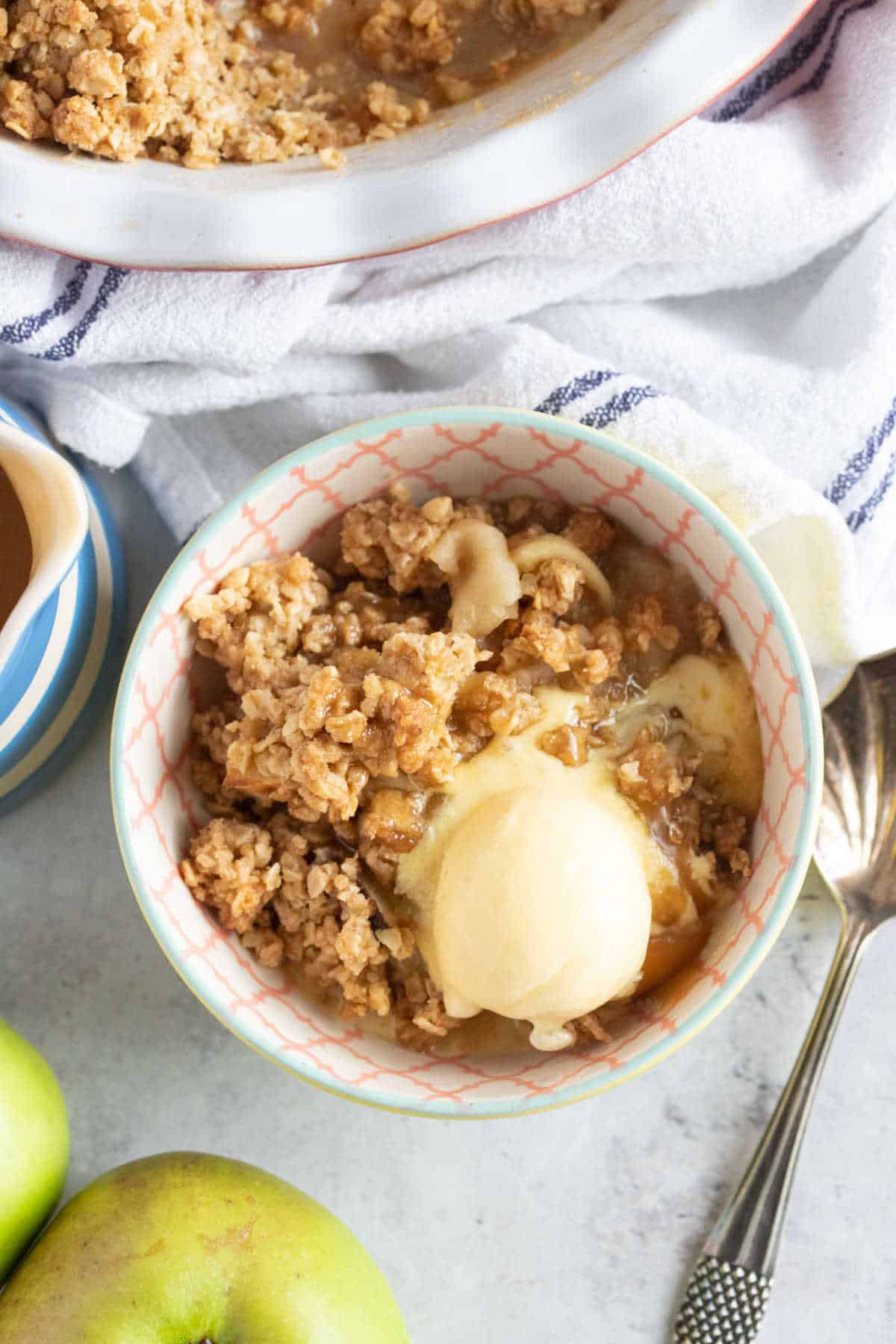 A bowl of toffee apple crumble with a scoop of vanilla ice cream on top.
