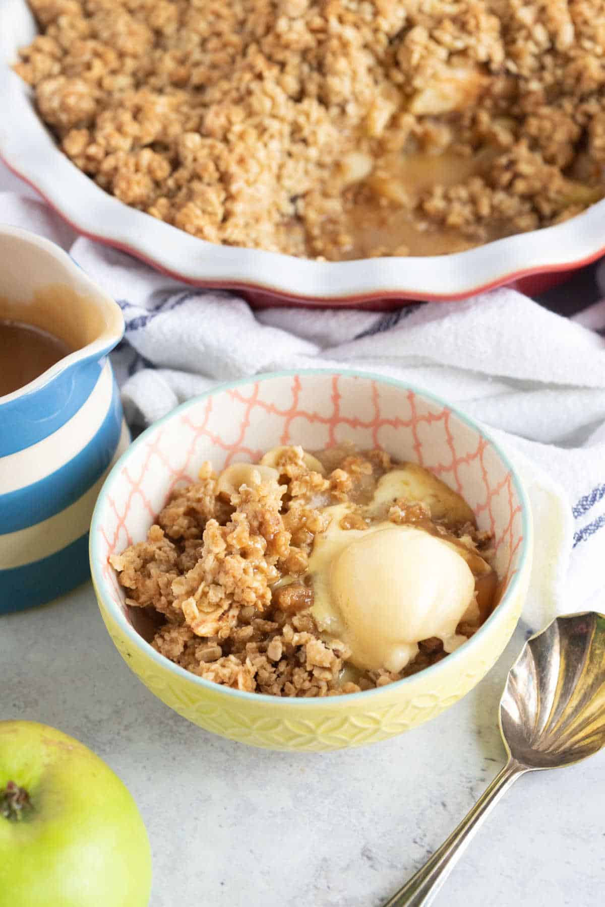 A bowl of toffee apple crumble with a jug of toffee sauce.