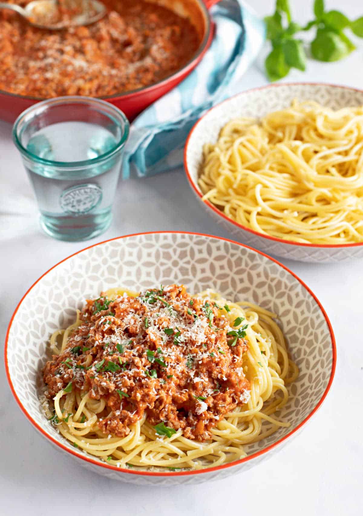 A bowl of turkey mince spag bol with a pan of bolognese sauce in the background.