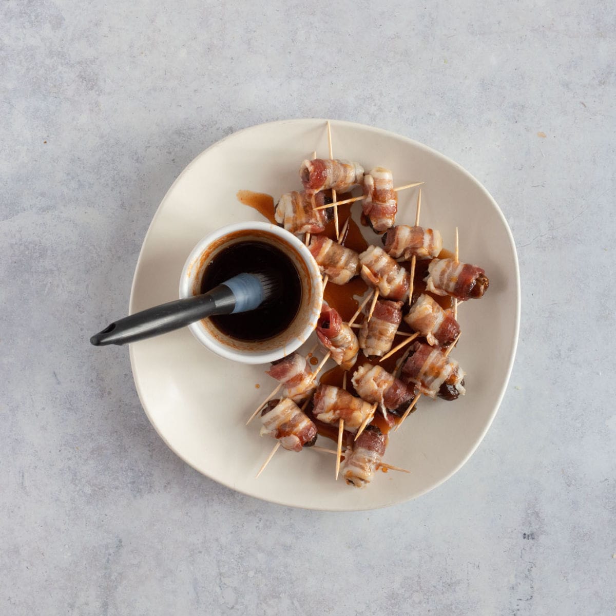 Uncooked devils on horseback on a plate ready to be brushed with the maple sriracha glaze.